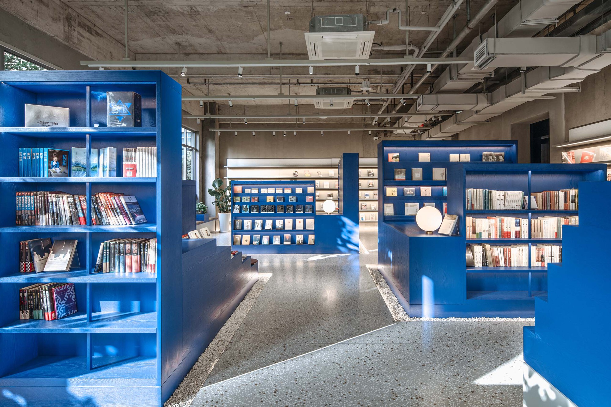Interior bookstore with blue freestanding shelving units and exposed concrete ceiling with visible mechanical systems