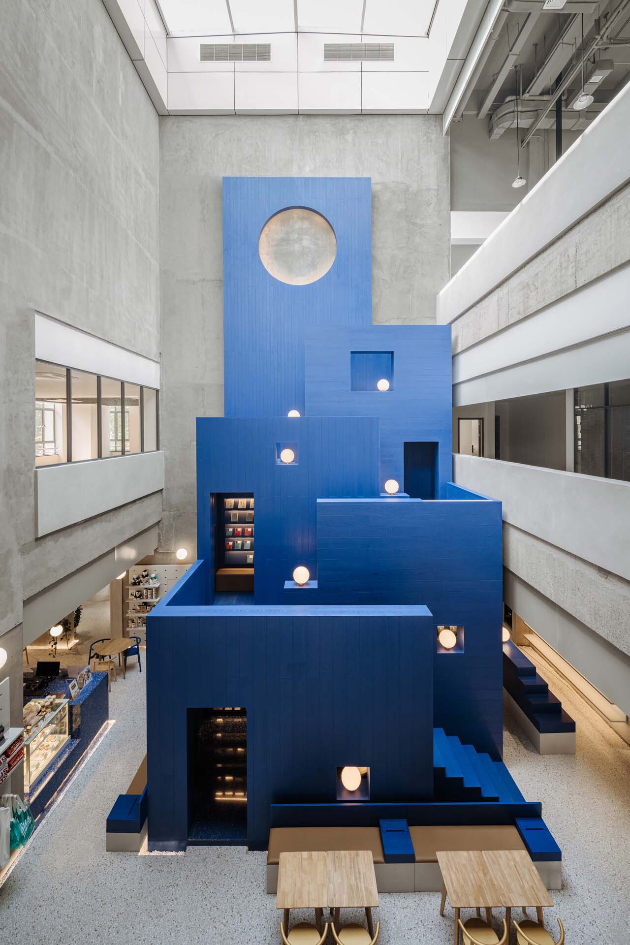 Multi-story atrium with a stepped blue staircase structure under a skylight with concrete balconies
