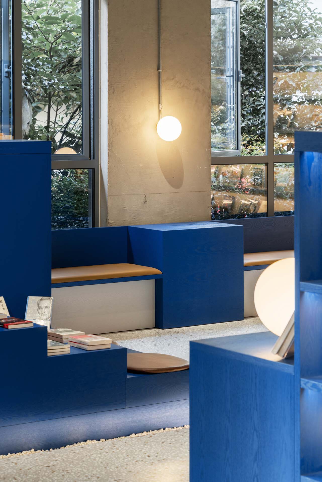 Blue seating platforms with spherical pendant lights beside floor-to-ceiling windows overlooking a courtyard