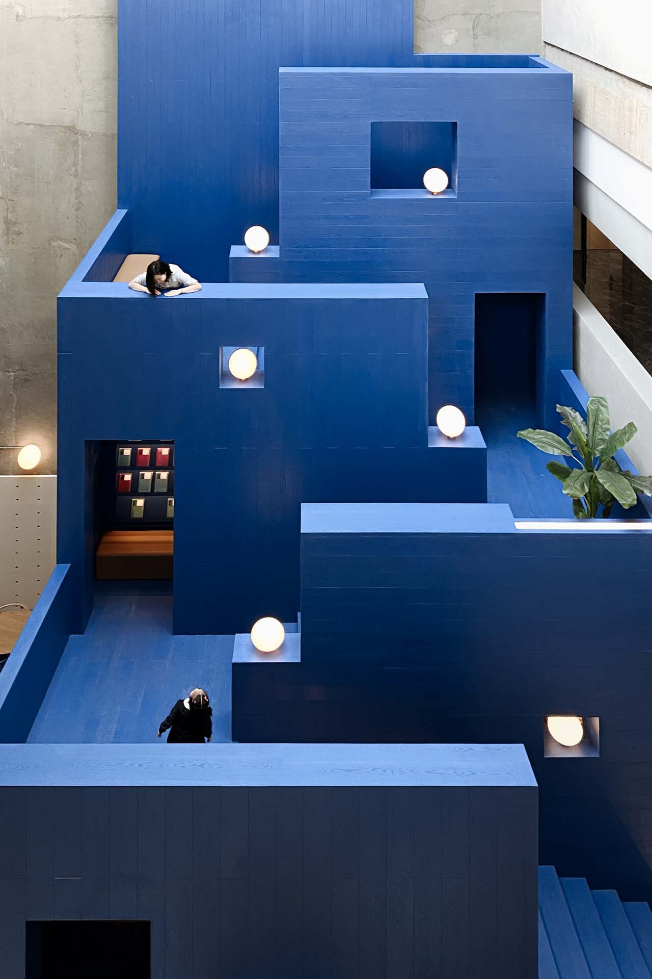 Stepped blue platforms with circular apertures, a lounging cat, and visitors exploring different levels