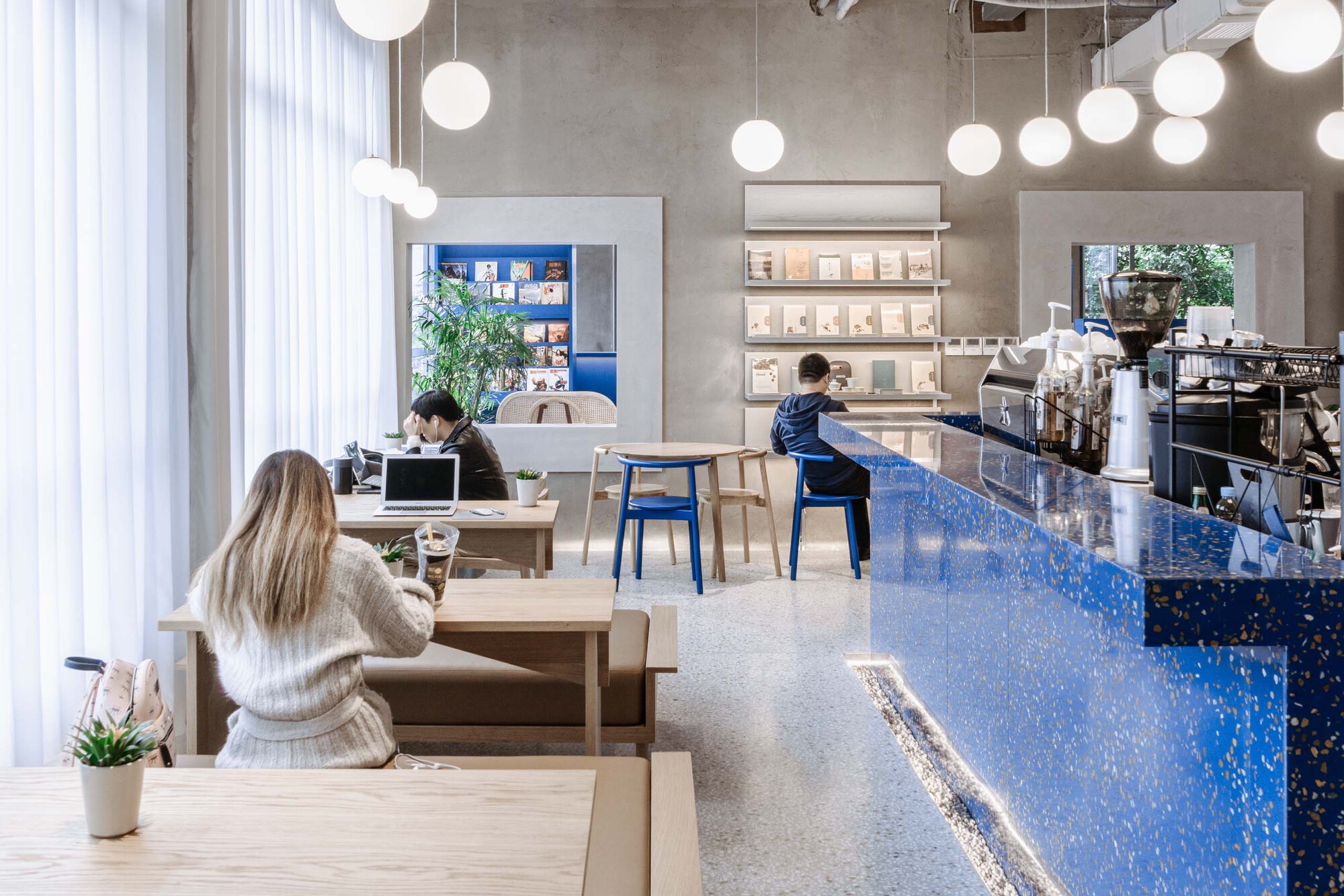 Cafe interior with blue terrazzo counter, white globe pendants, and patrons at timber tables