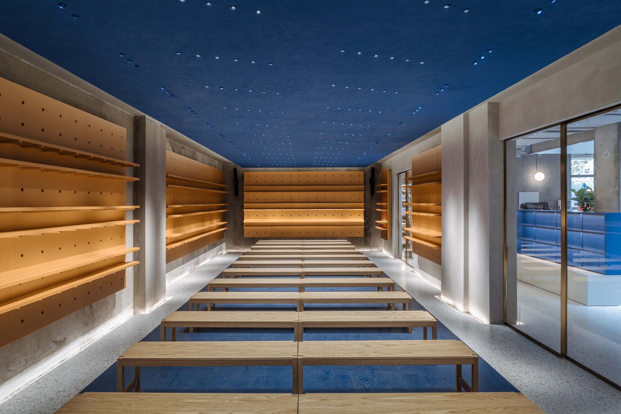 Interior retail space with timber display shelves, benches, and a perforated blue ceiling lit from above