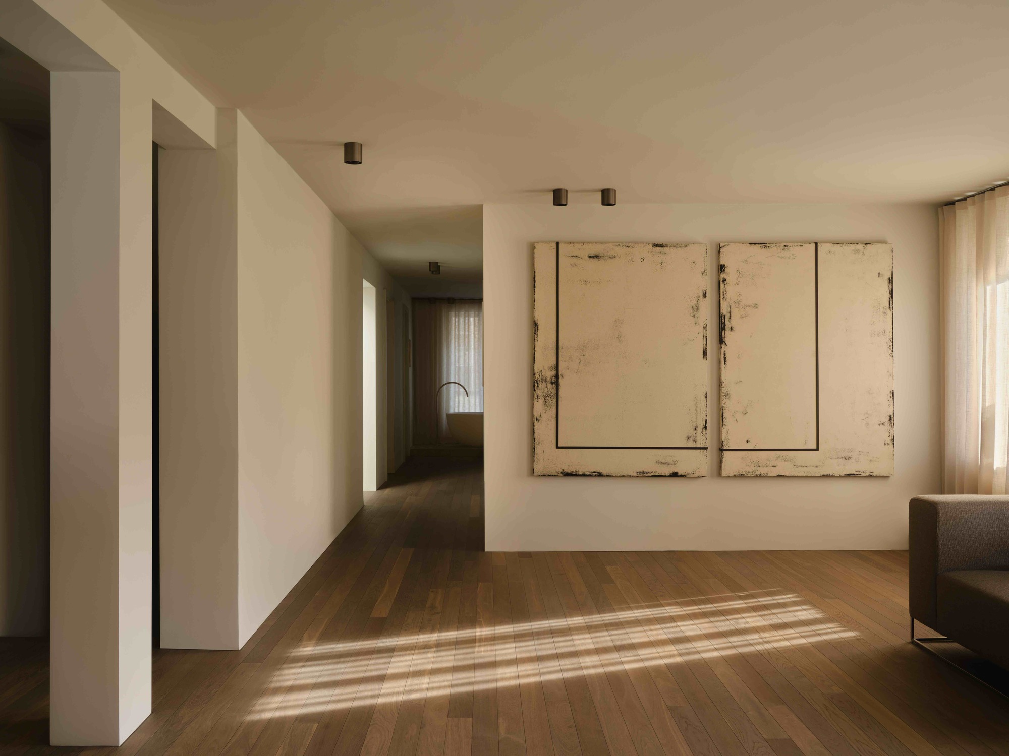 White corridor with recessed doorways and striped sunlight falling across timber floorboards