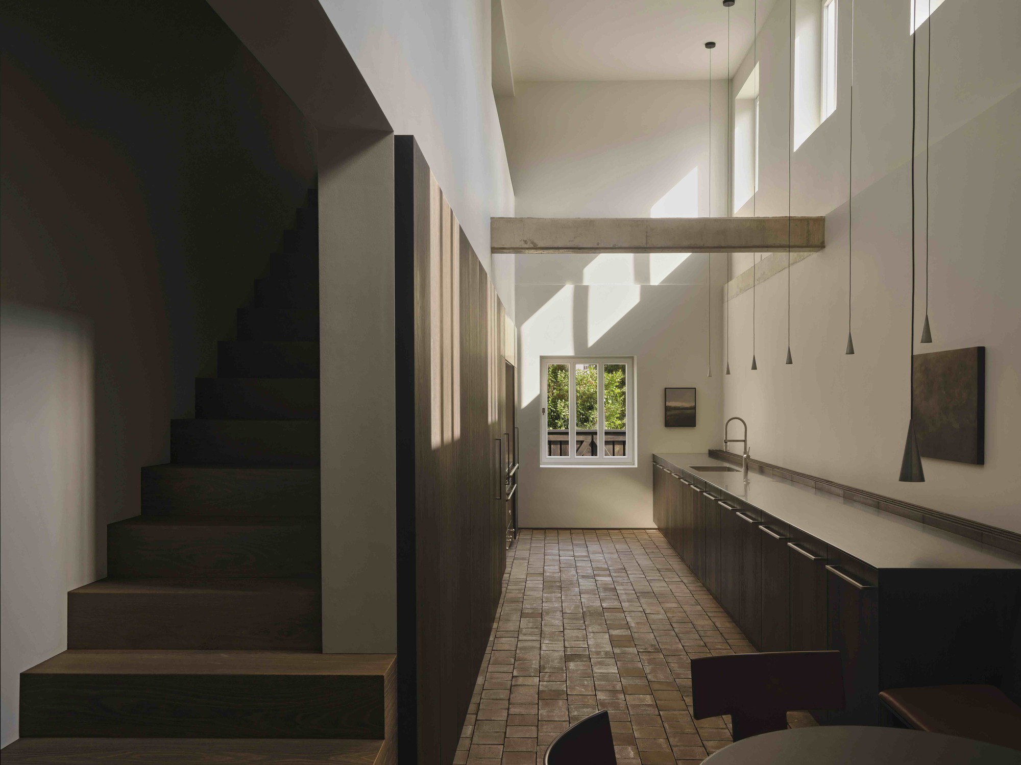 Double-height kitchen with dark timber stair and pendant lights above tiled floor