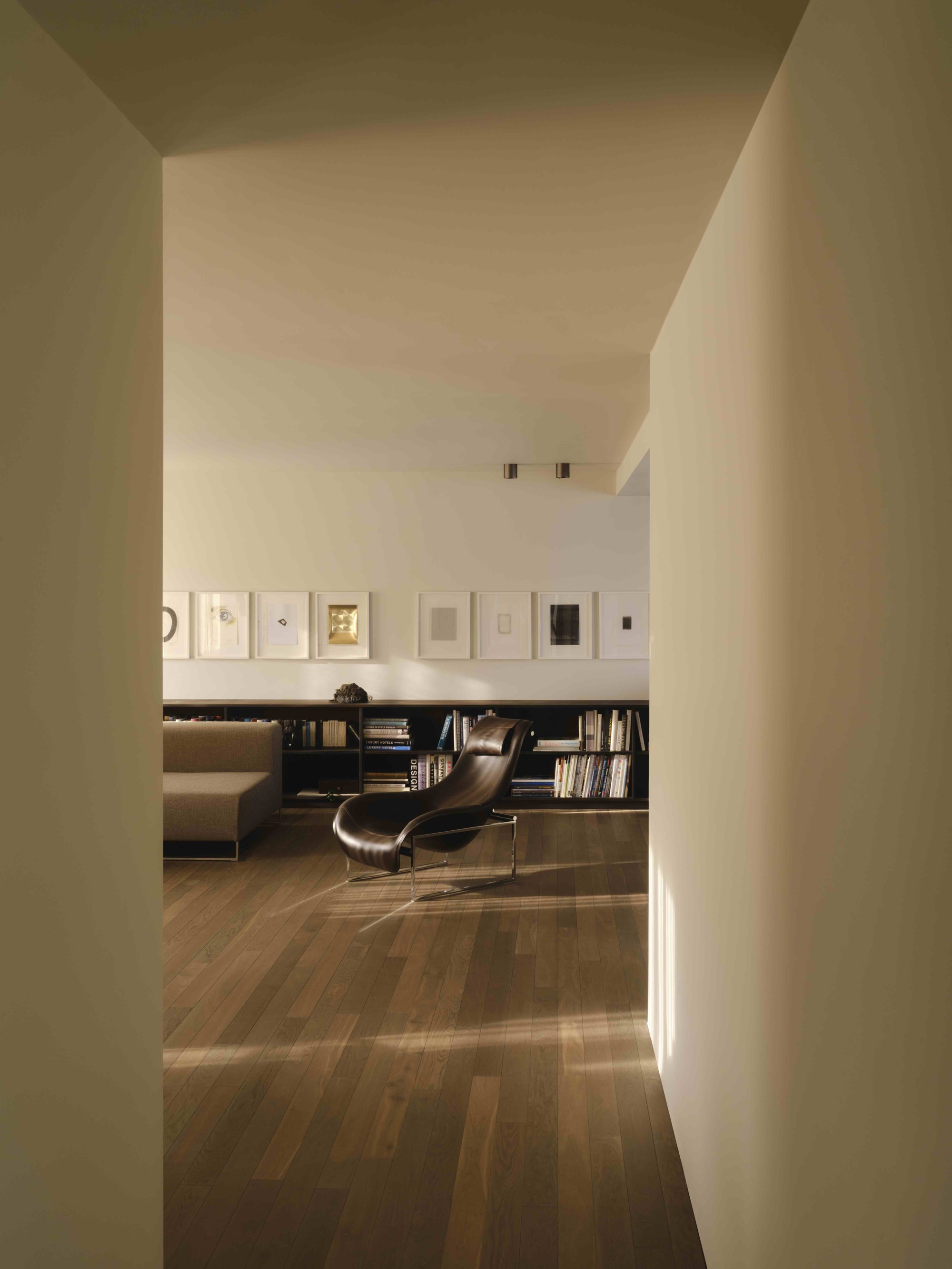 View through white plastered columns into a reading room with framed artworks and low bookshelves