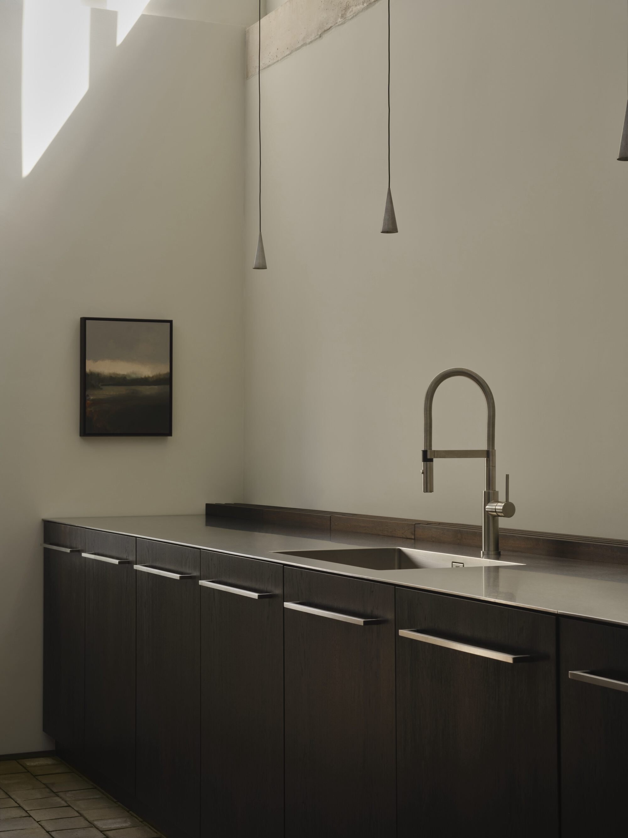 Dark timber kitchen cabinetry with stainless steel countertop and conical pendant lights above terracotta tile floor