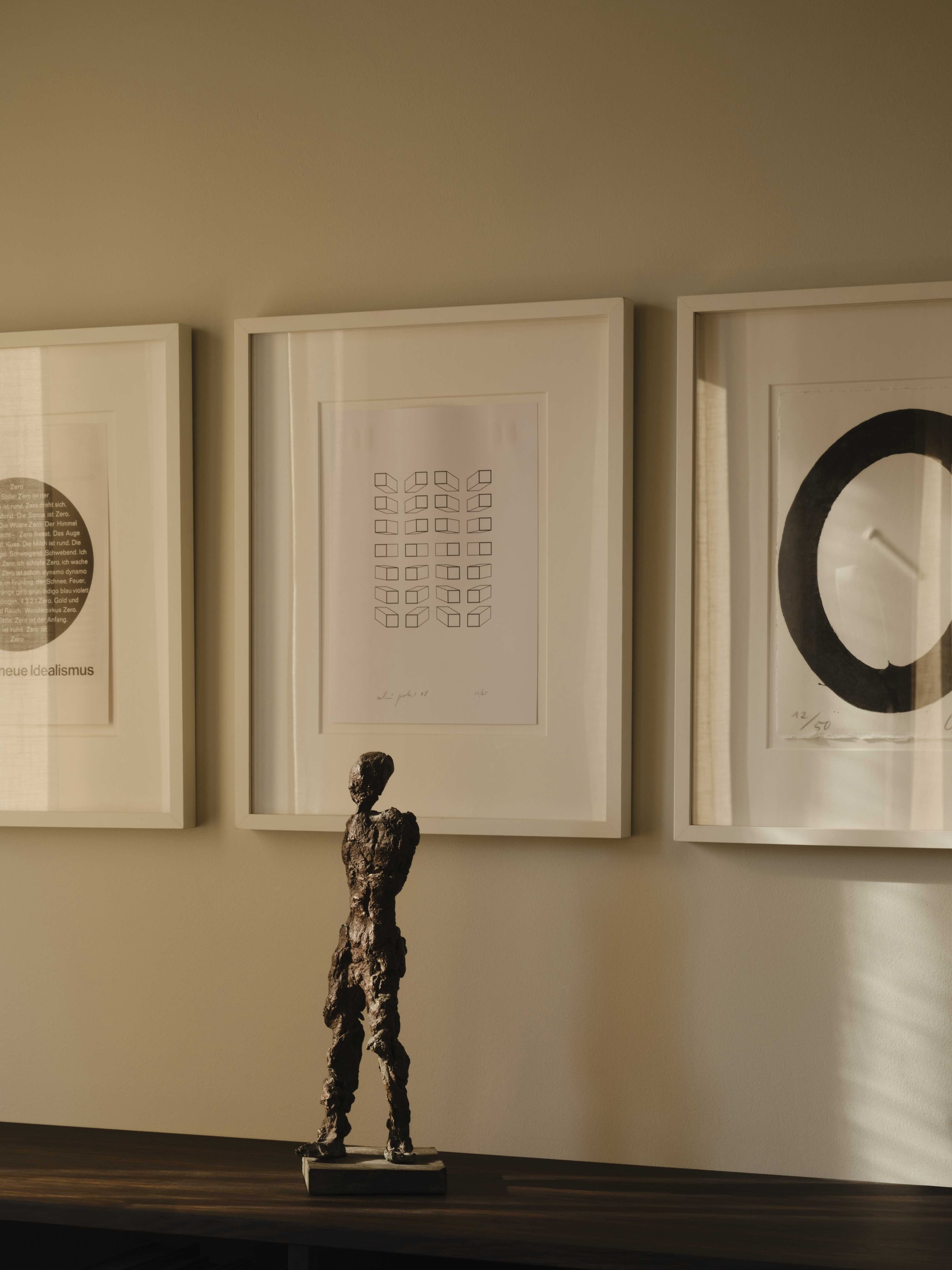 Bronze figure sculpture on a dark timber shelf beneath three framed artworks in afternoon light