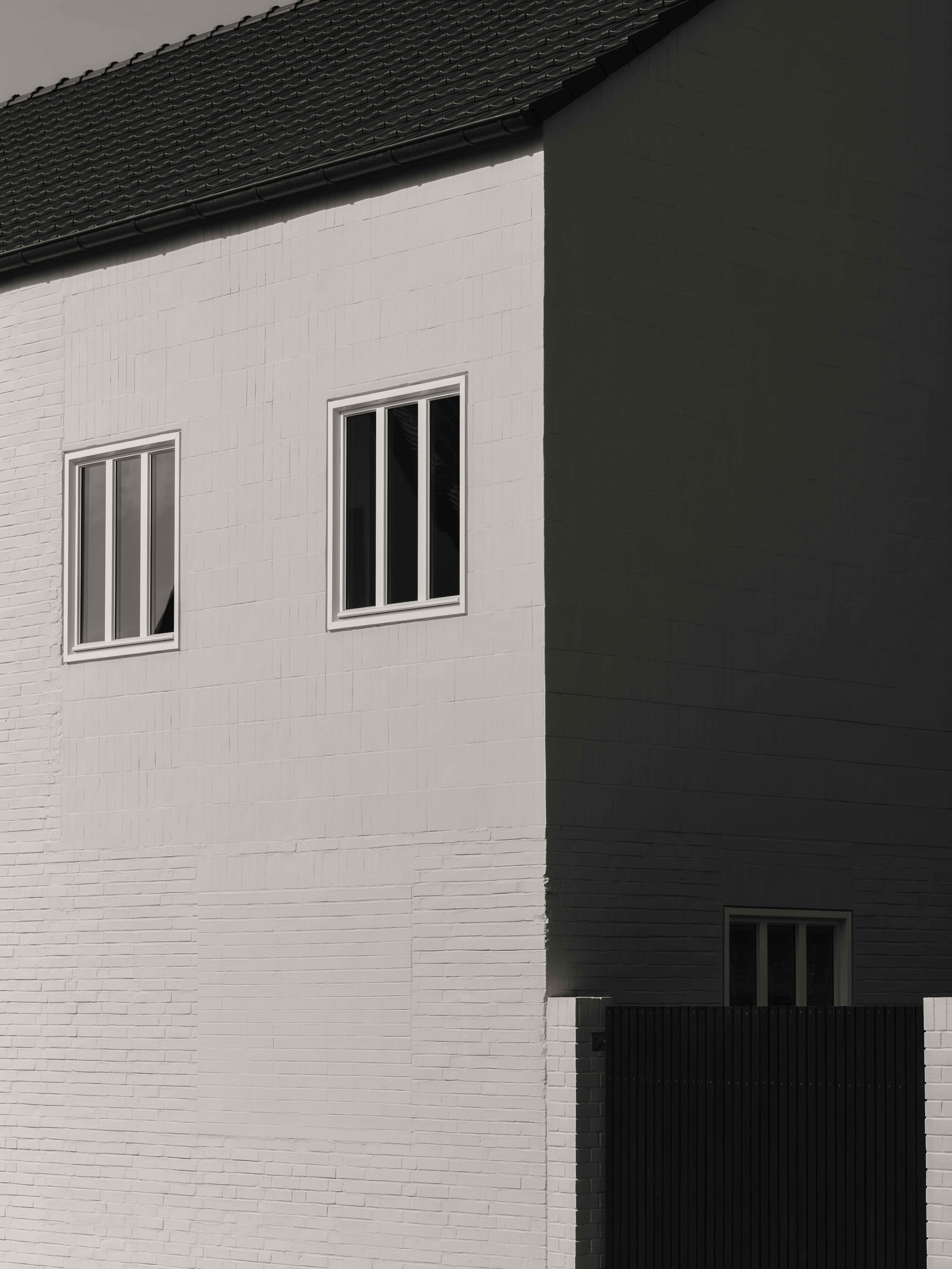 Junction of white painted brick and dark brick facades with triple vertical windows and pitched roof