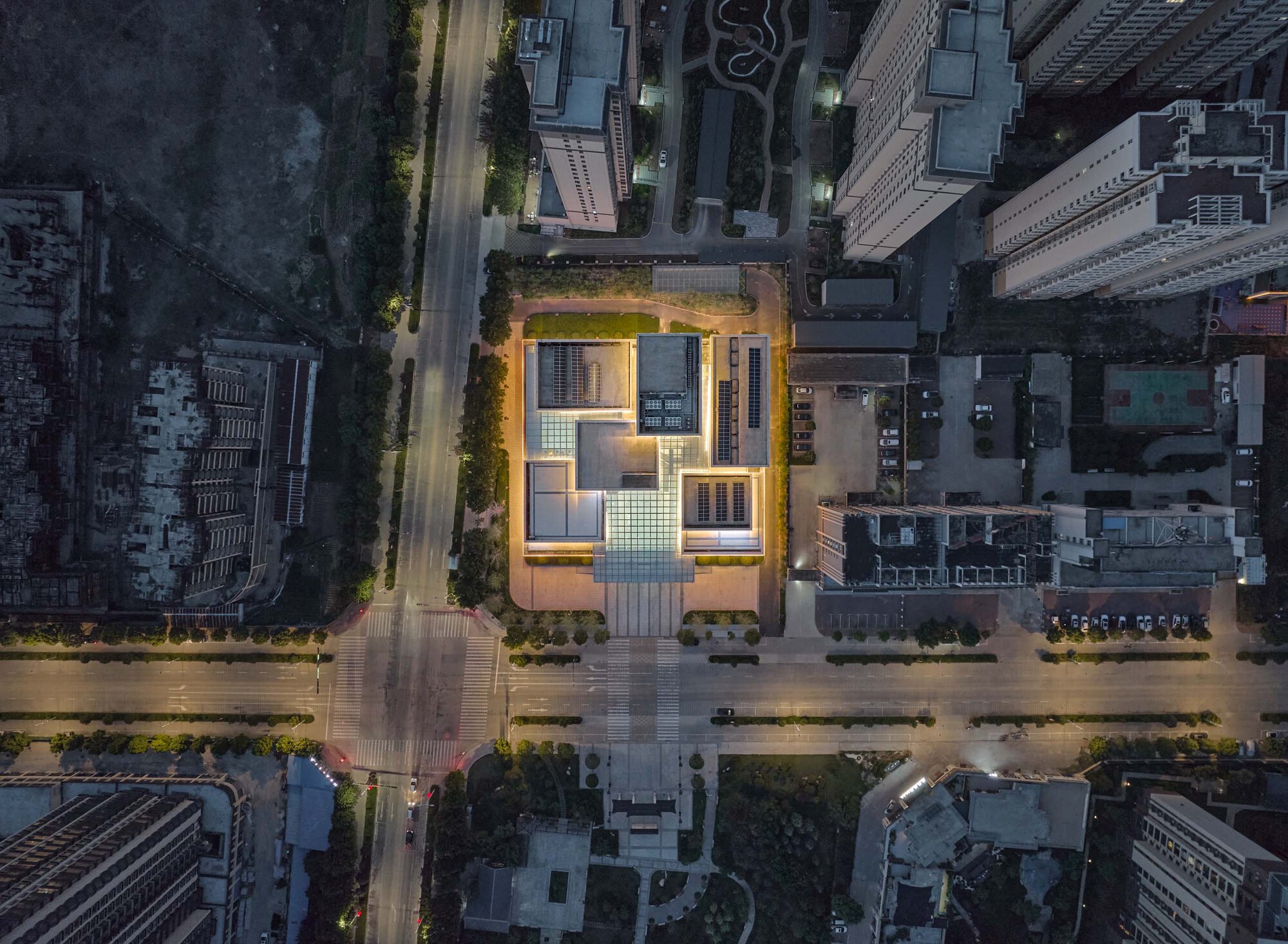 Aerial view at dusk of the illuminated rooftop courtyard surrounded by dense urban blocks