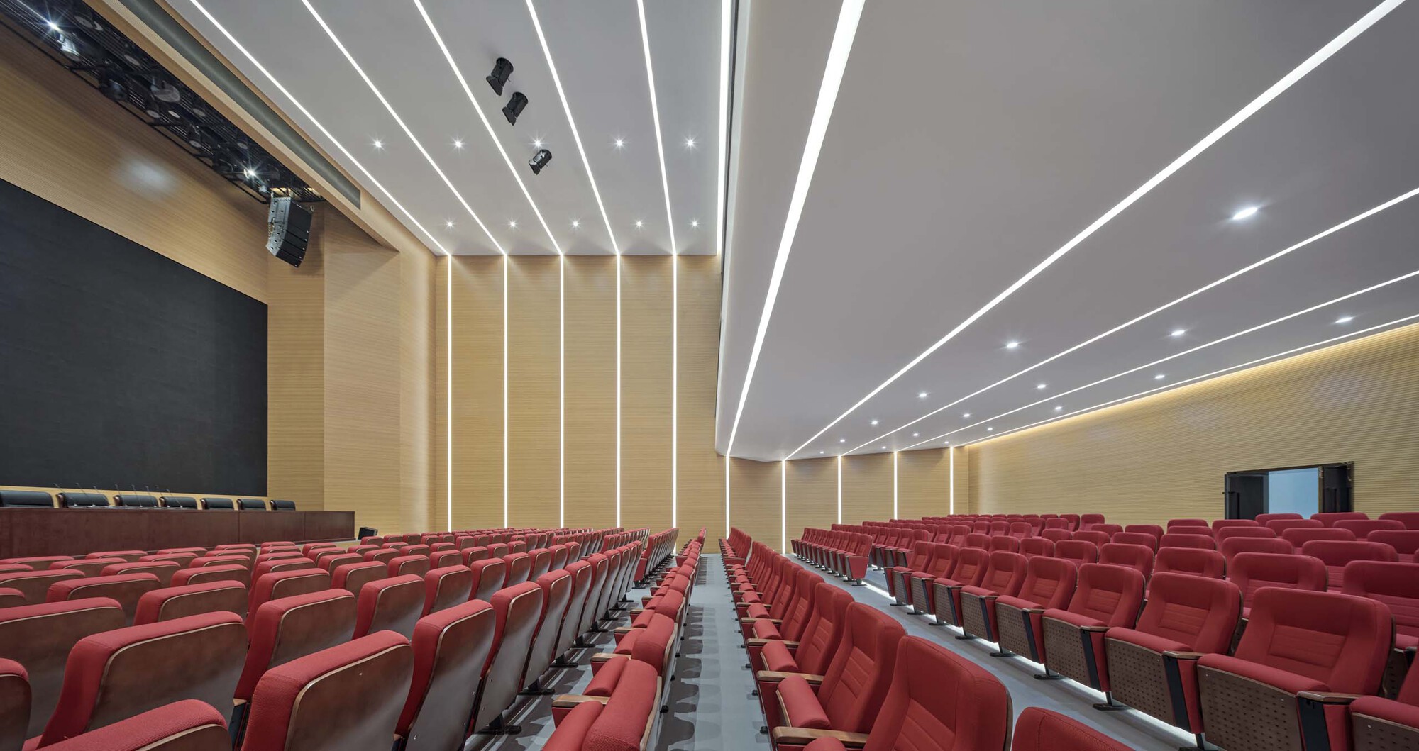 Auditorium interior with red seating rows and linear ceiling light strips