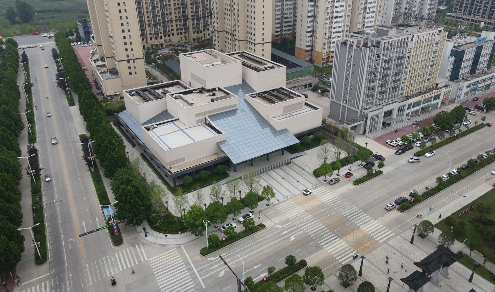 Aerial view of the low-rise complex with glazed roof among residential towers and tree-lined streets