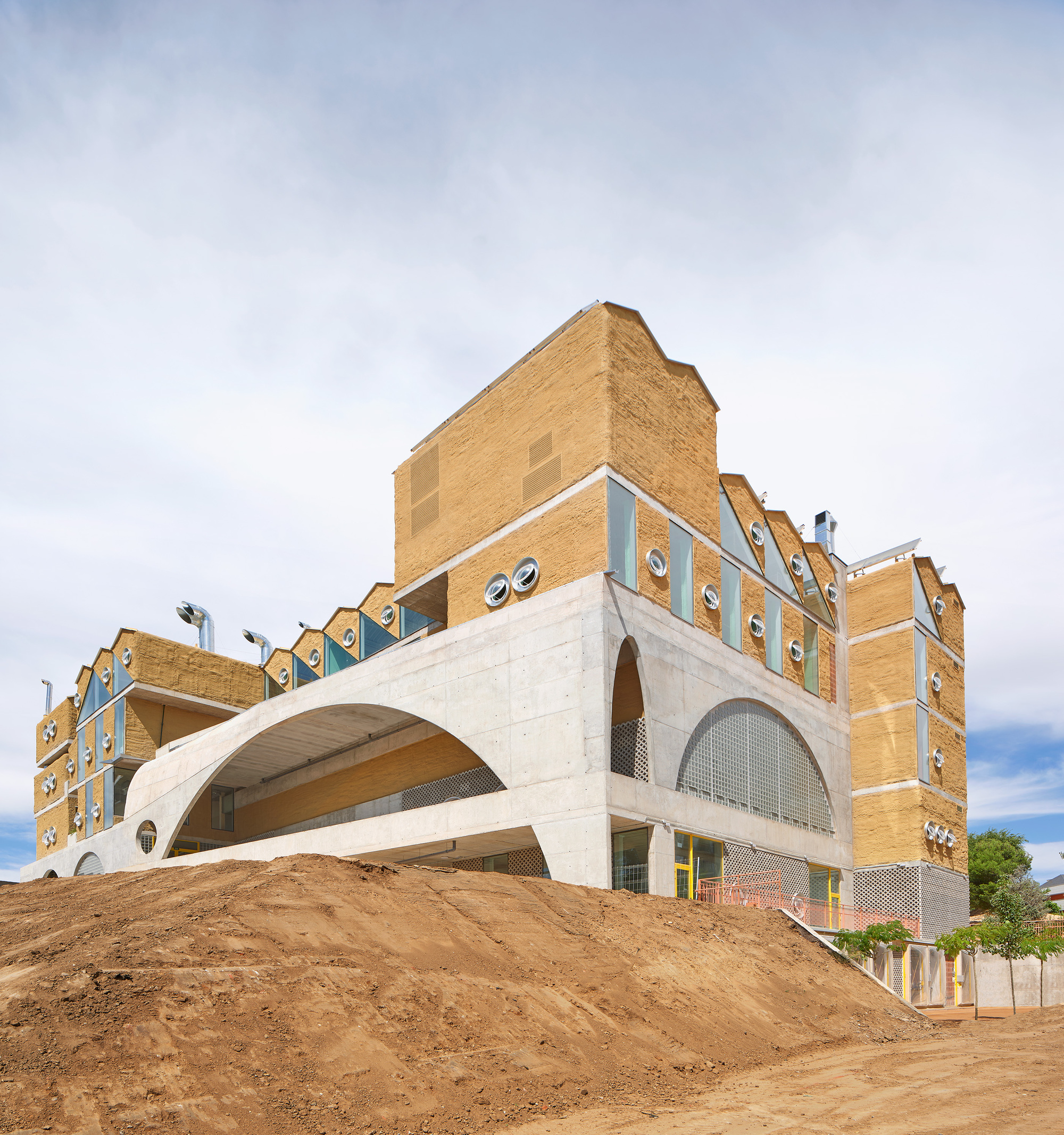 Side view of the concrete arch and sloped earth berm beneath stepped brick volumes with porthole windows