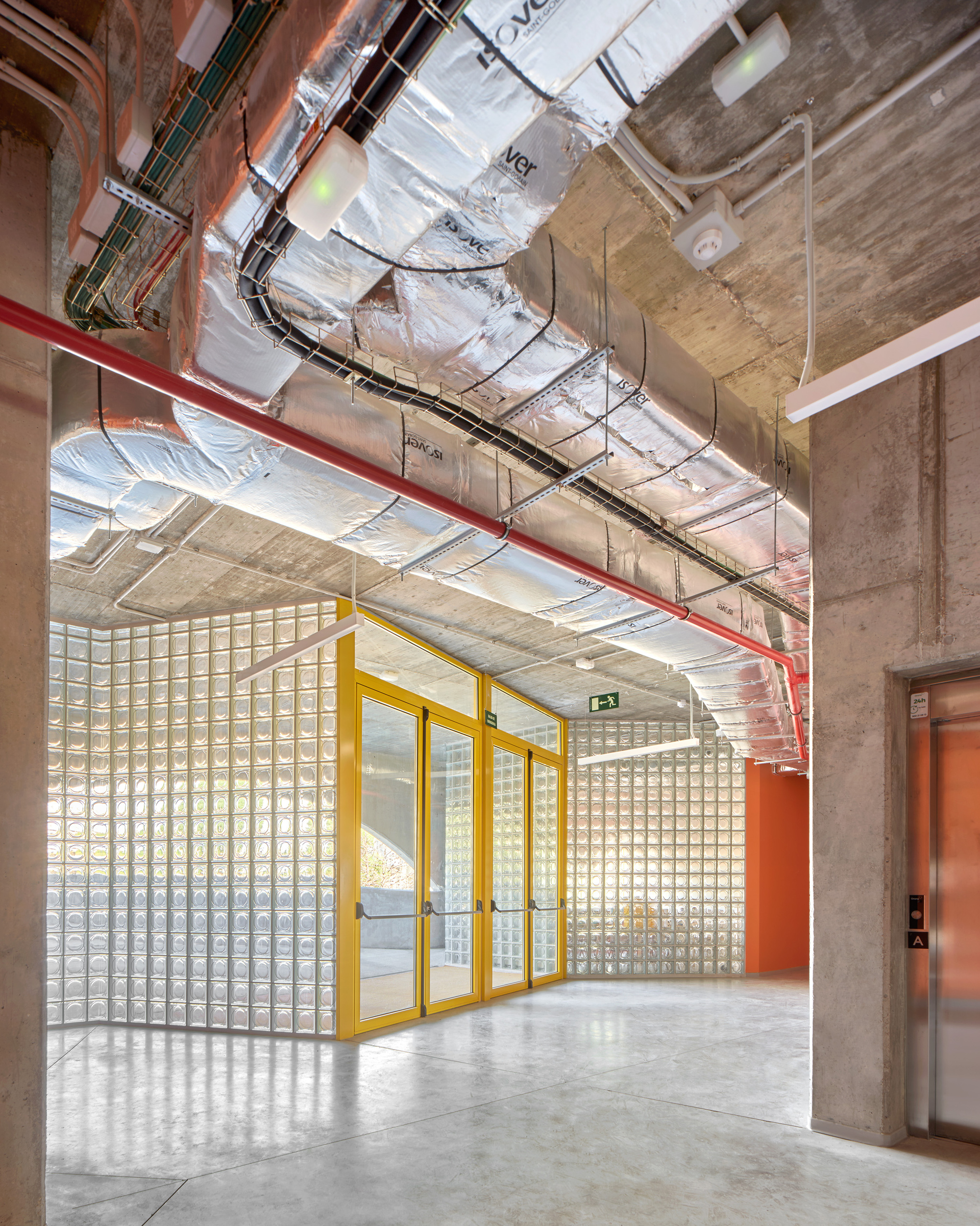 Circulation hallway with exposed ductwork and yellow-framed glass block partition wall