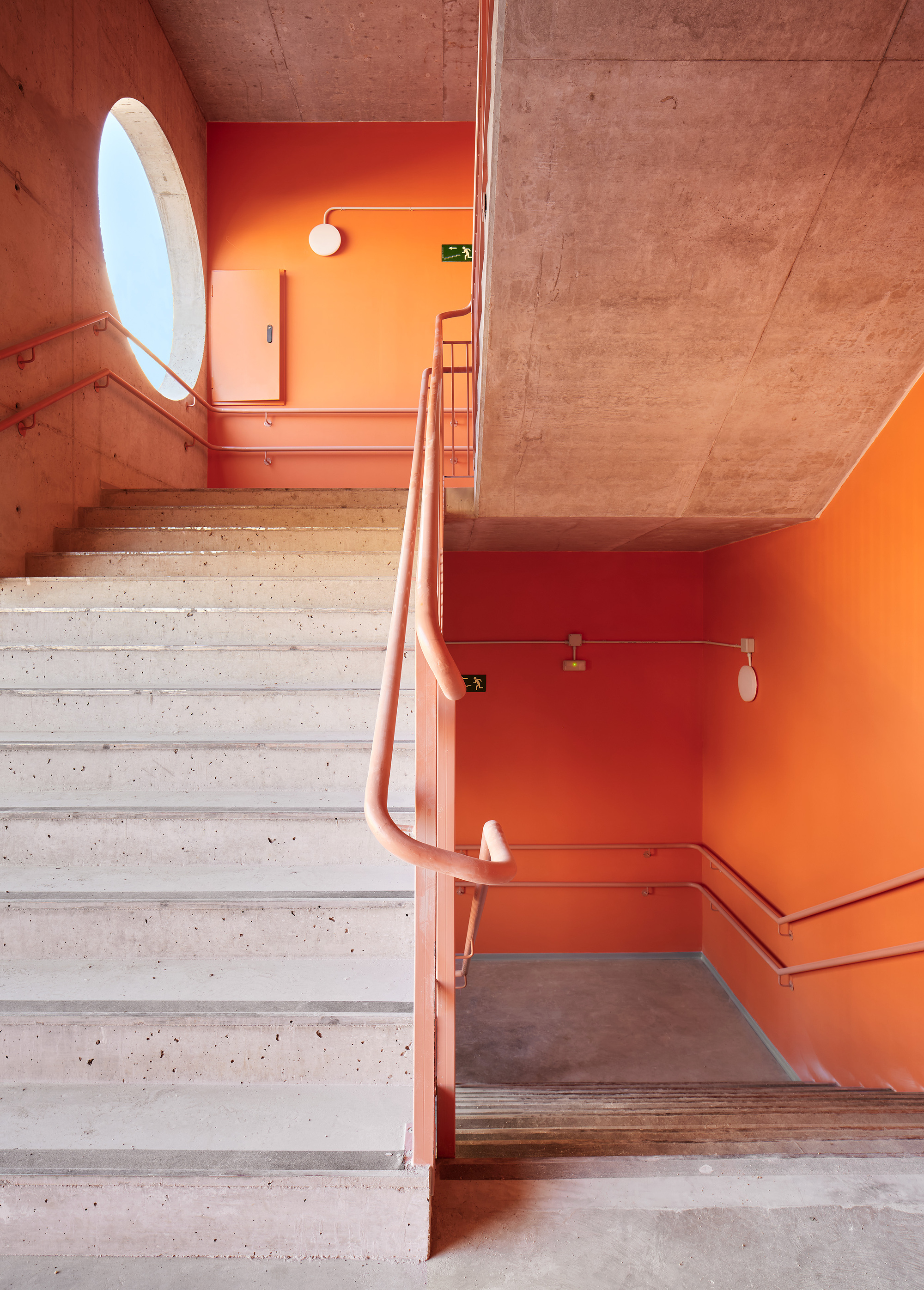 Concrete staircase with circular window and tubular steel handrail against orange painted walls