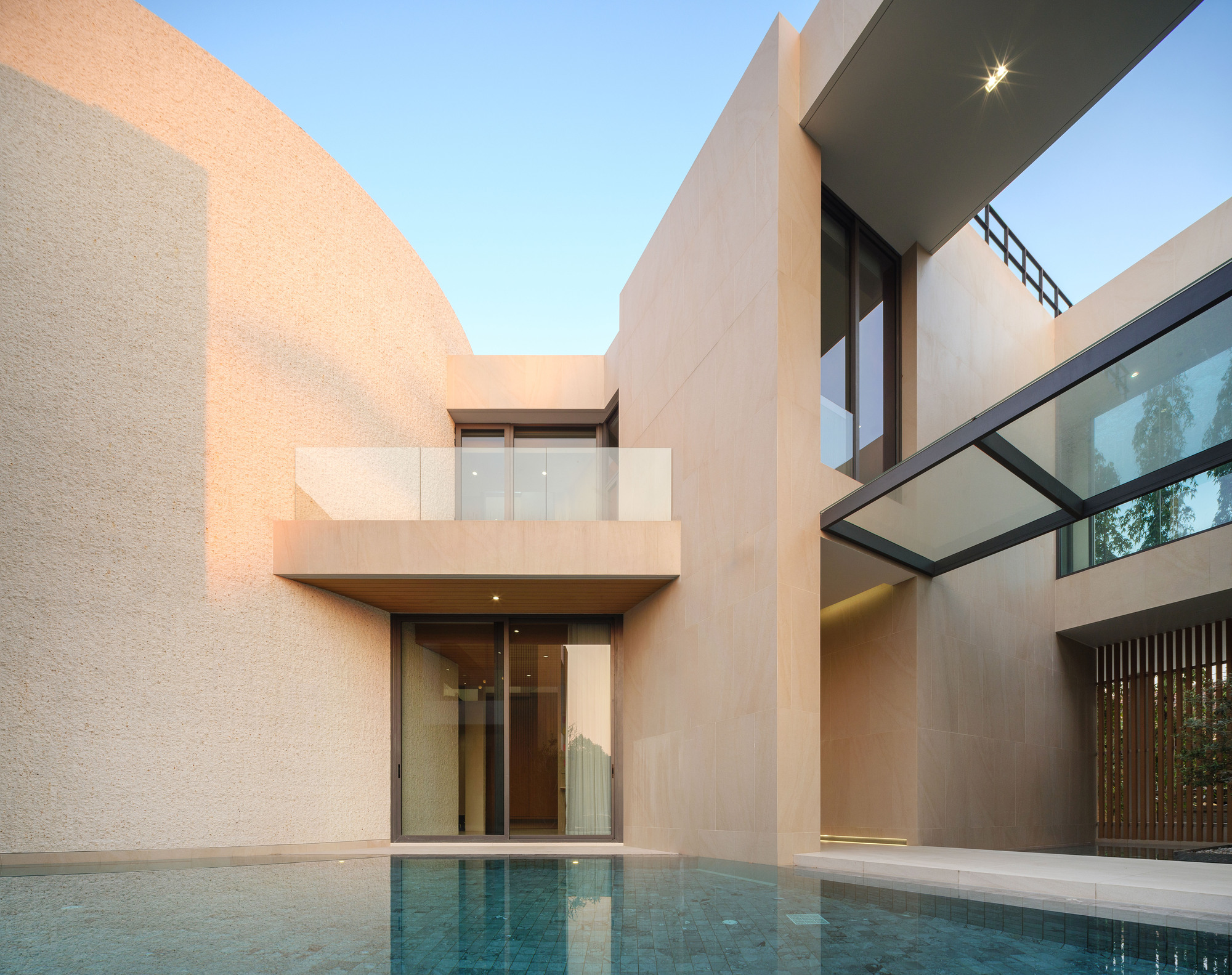 Courtyard pool at dusk with cantilevered balcony and floor-to-ceiling glazed entrance below
