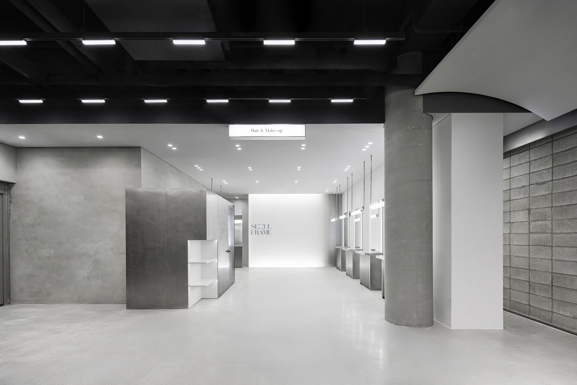 Retail corridor with cylindrical concrete columns, black coffered ceiling and recessed linear lighting