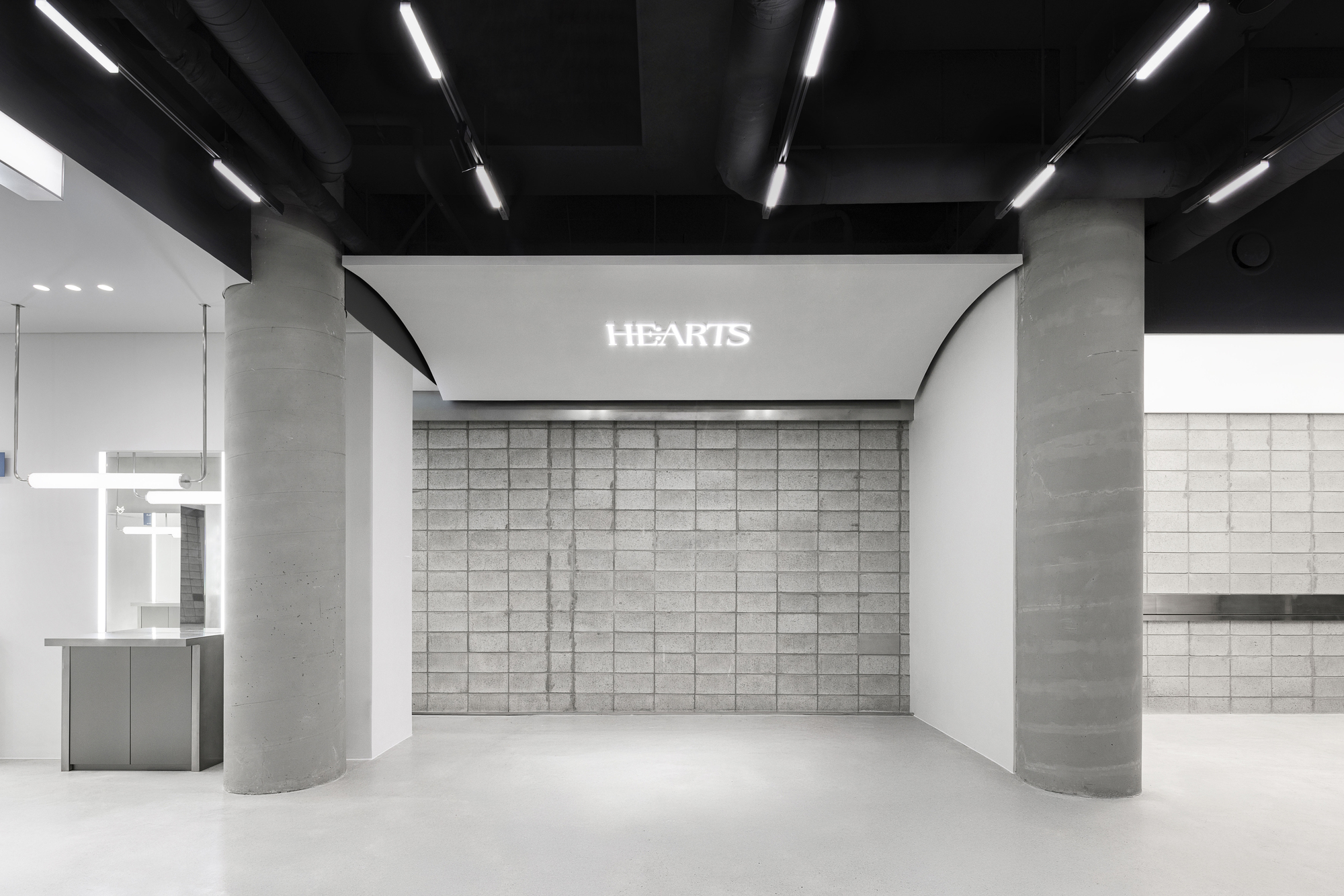 Gridded concrete block wall with illuminated signage flanked by cylindrical concrete columns