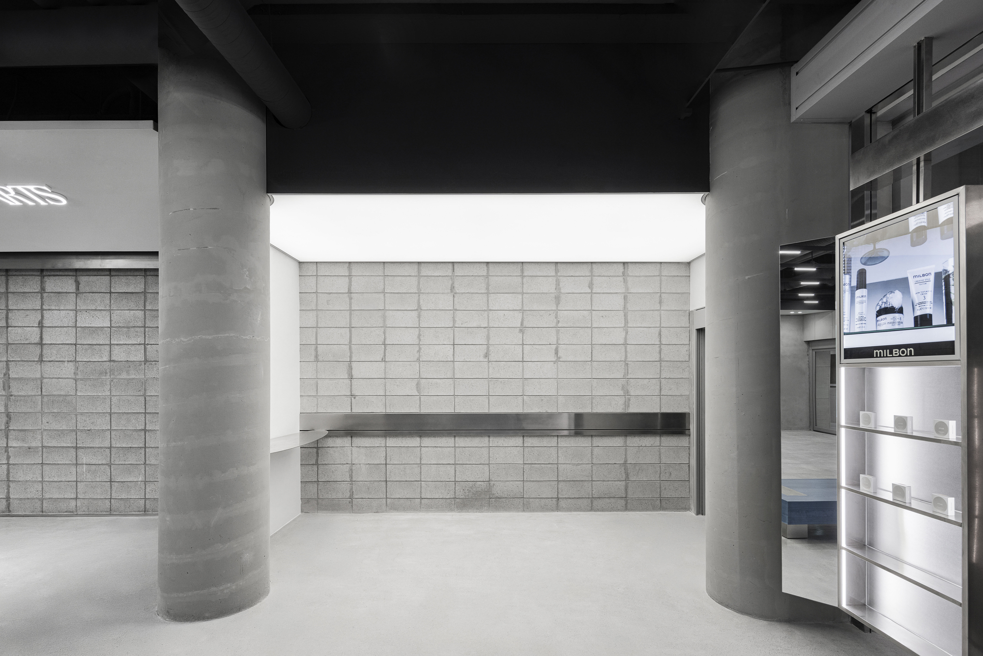 Display alcove with gridded block wall, floating shelf and cylindrical concrete columns under black ceiling
