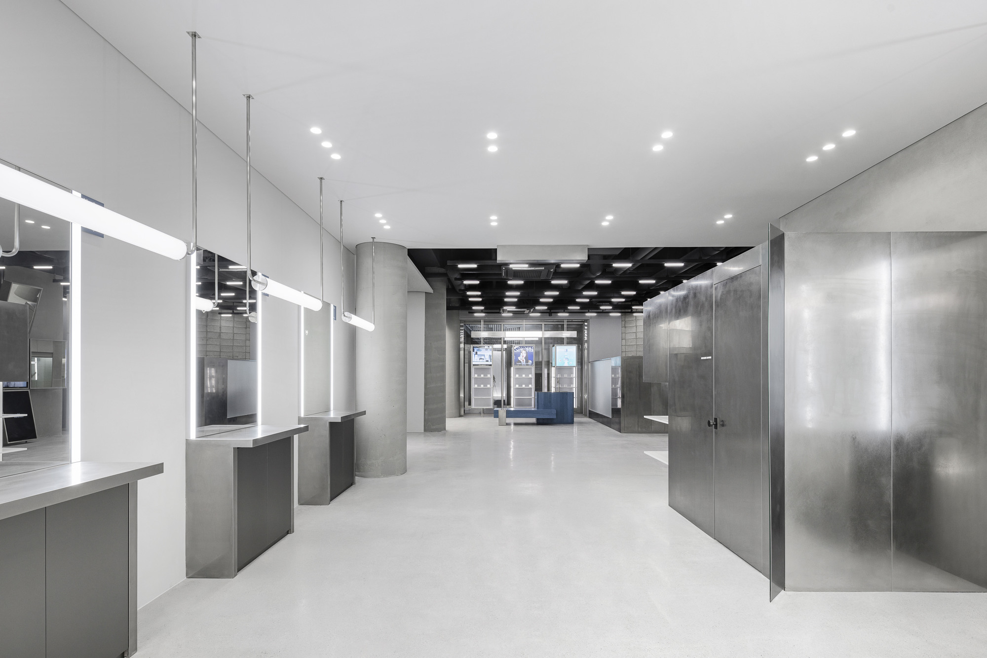 Interior retail space with suspended glass display cases, concrete walls and grid ceiling with recessed lights