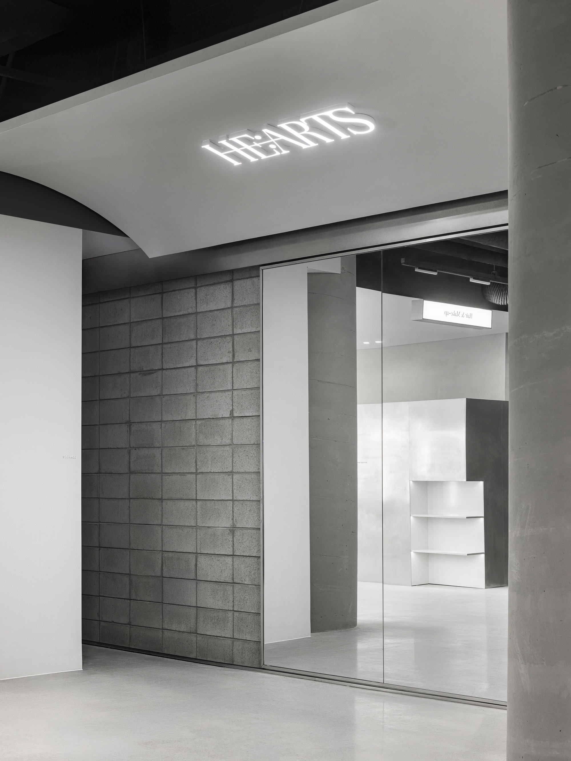 Glass storefront entrance with illuminated ceiling logo and view into retail space with white stepped displays