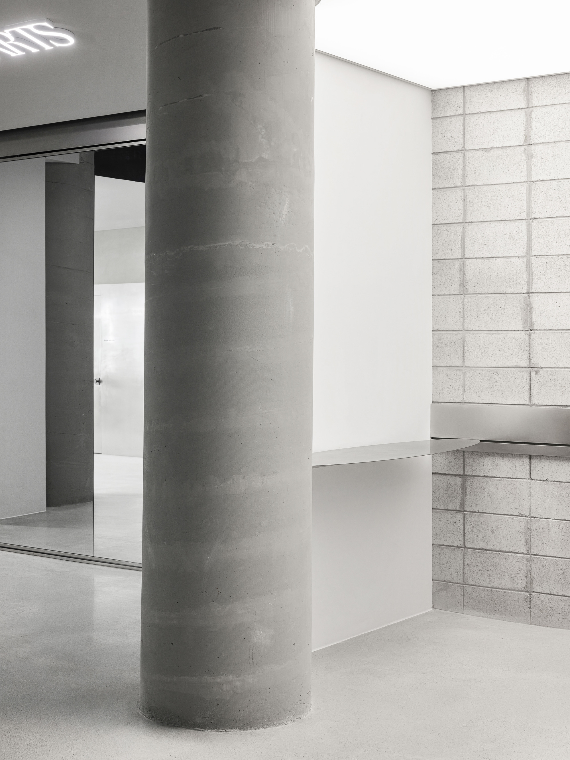 Concrete column in a white-walled interior with gridded stone block wall and polished floor