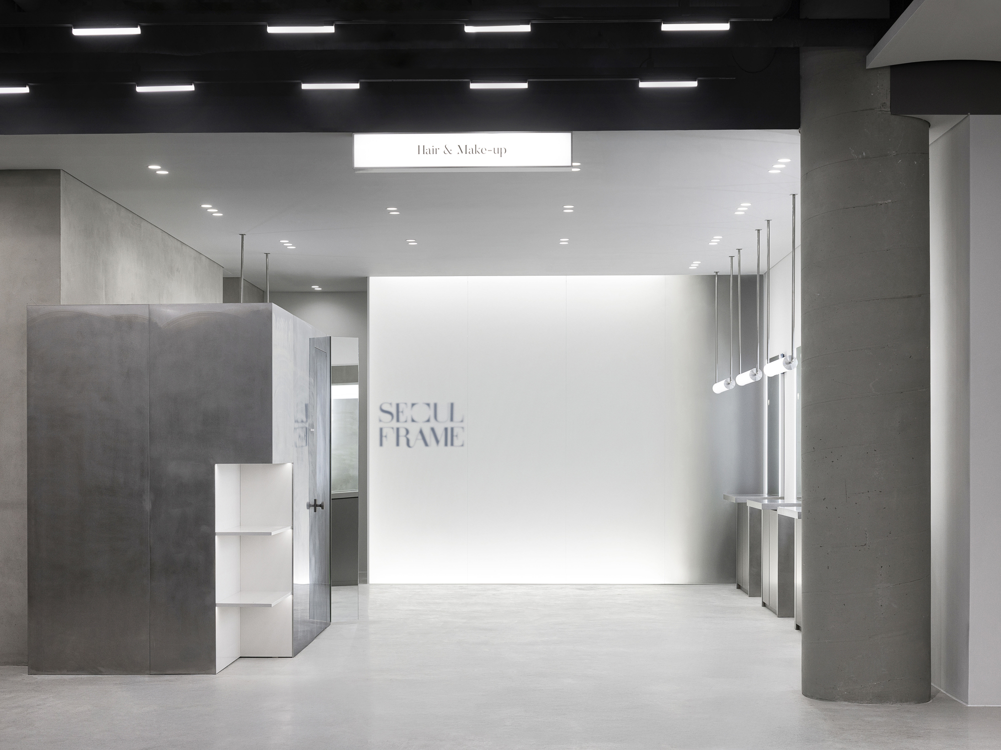 Retail interior with concrete columns and white wall displaying signage under linear ceiling lights
