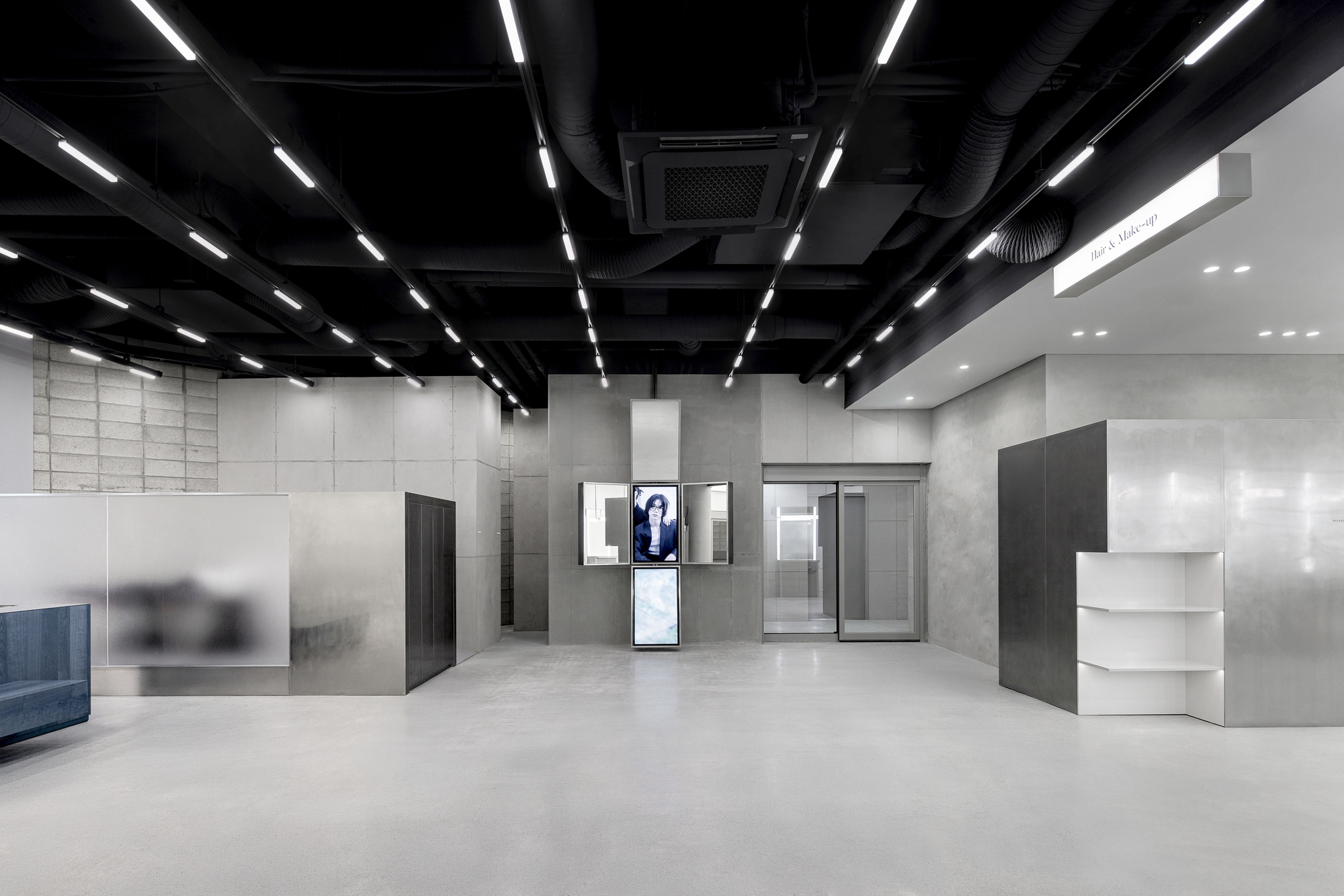 Open commercial space with exposed black ceiling ducts and linear lighting above display screens