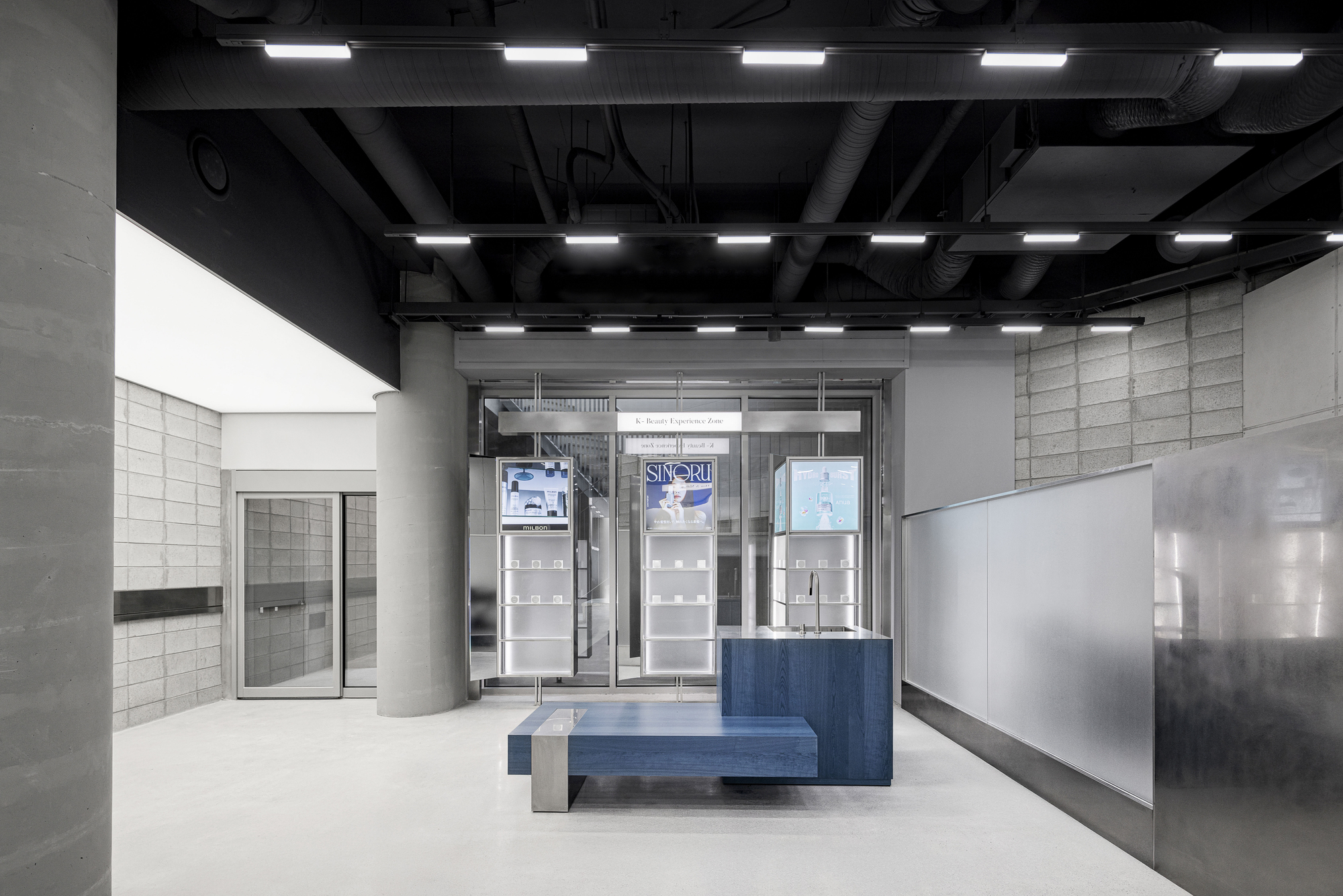 Blue wood bench and counter facing glazed storefront under exposed structural ceiling and lighting