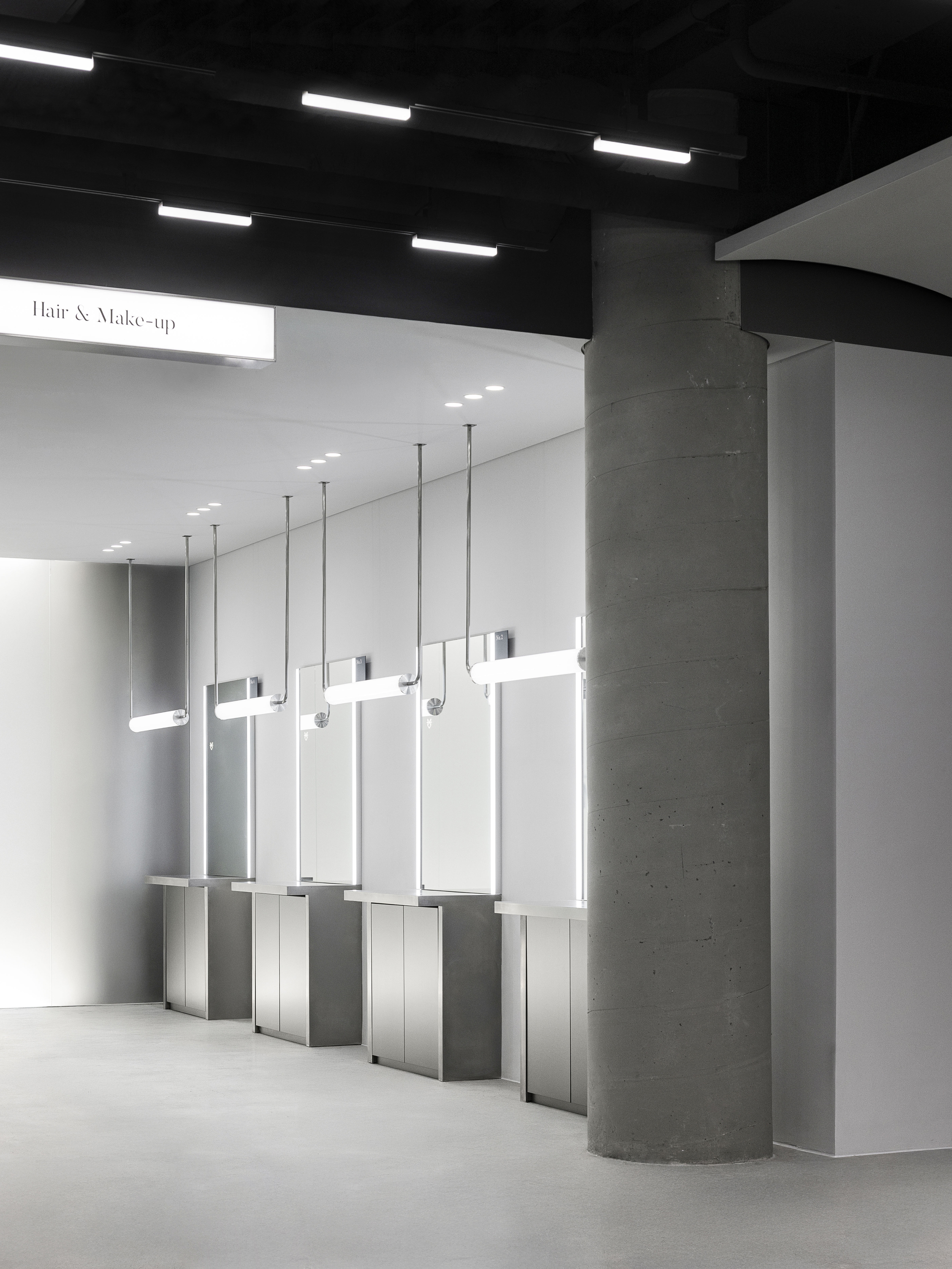 Row of backlit mirrors suspended from the ceiling with circular concrete columns against white walls