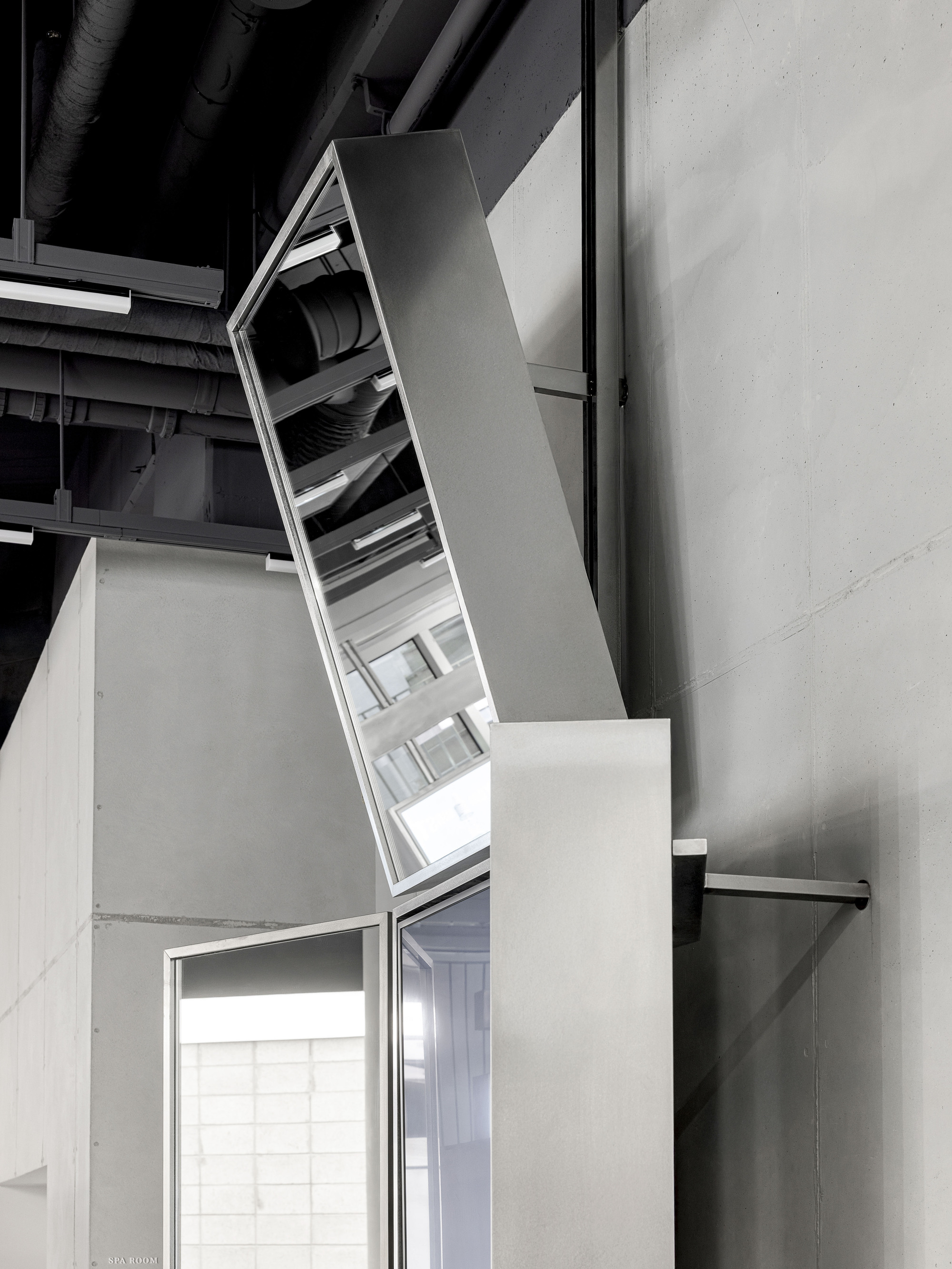 Angled skylight penetrating through white volume beneath exposed black ceiling ductwork
