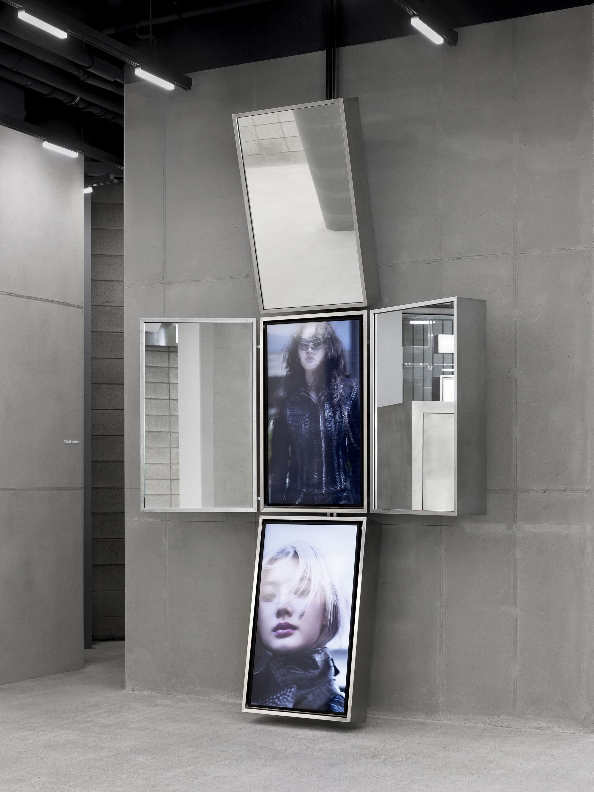 White display unit with pivoting screens showing portrait images against concrete panel walls