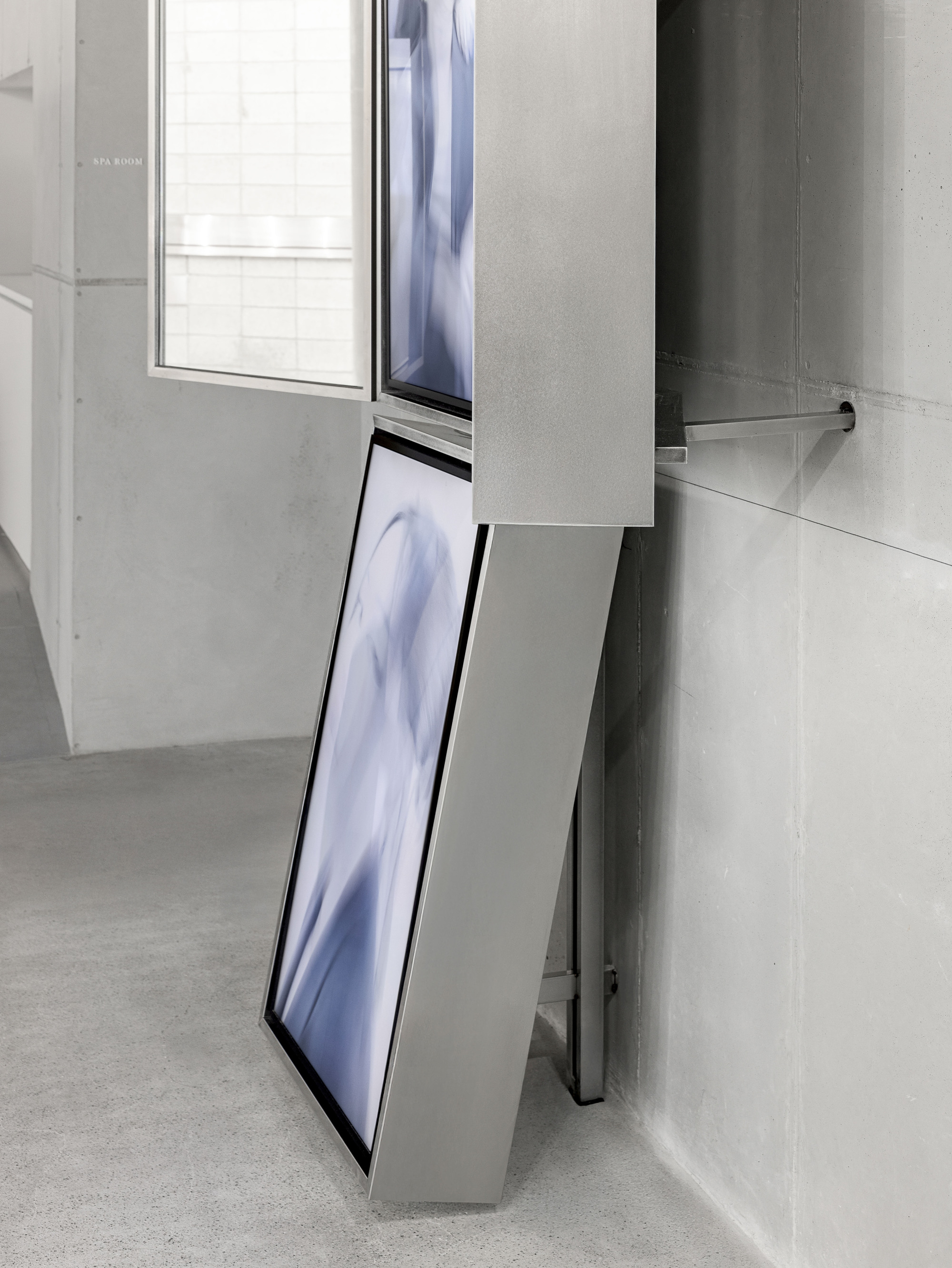 Tilted digital screen mounted to white volume beside window opening in concrete wall