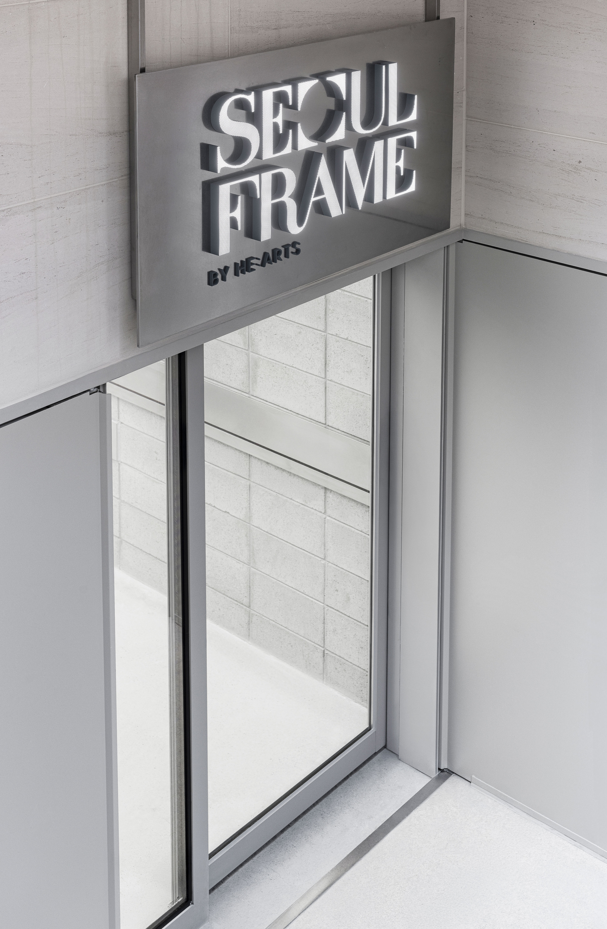 Glass entrance with aluminum frame beneath an overhead signage panel and pale tiled walls