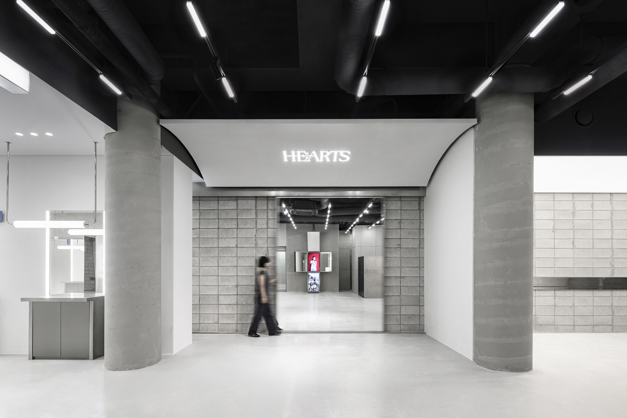 Interior hall with concrete columns and black exposed ceiling beams as a person walks through