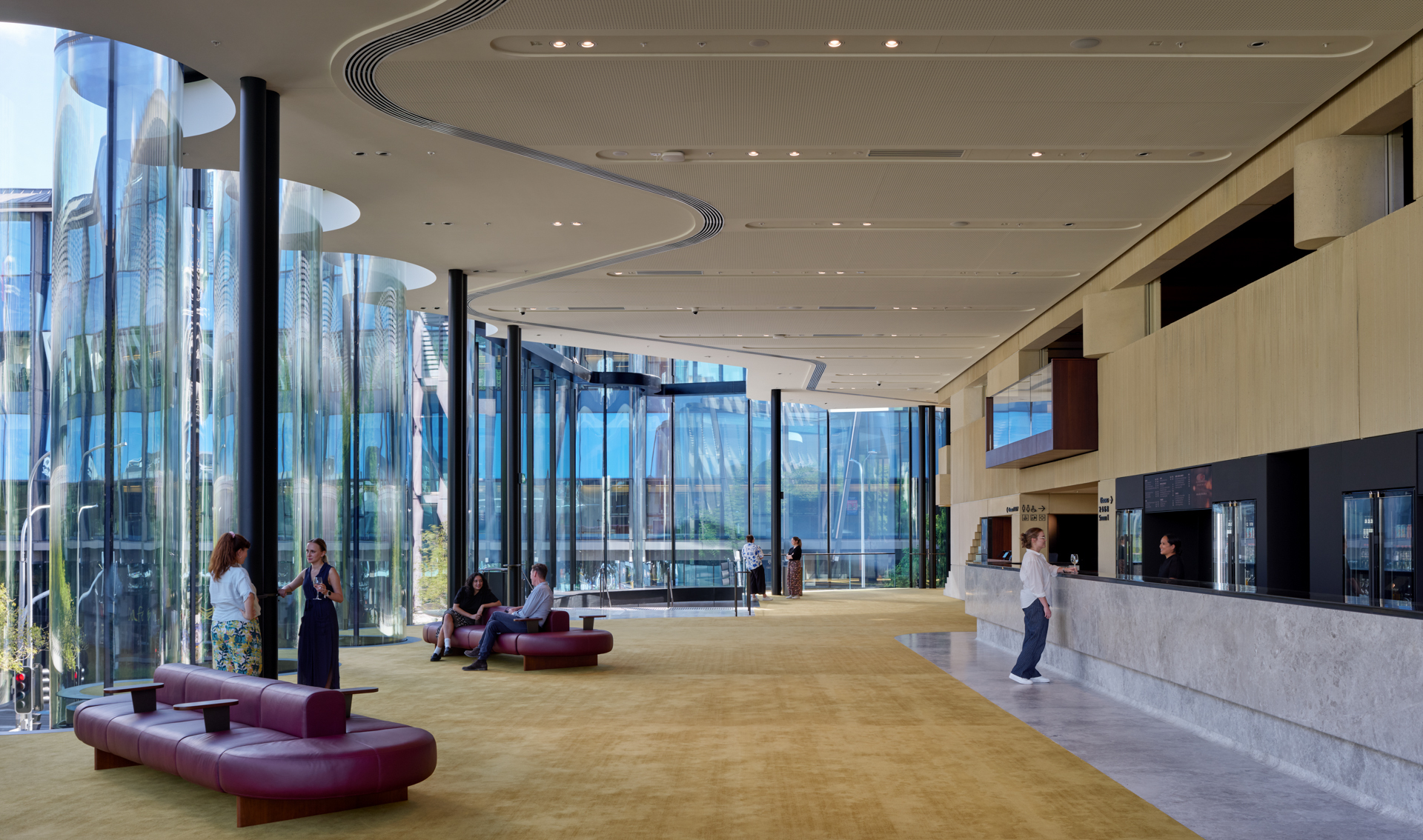 Interior lobby with curved ceiling lighting strips, full-height glazing, and red modular seating with visitors