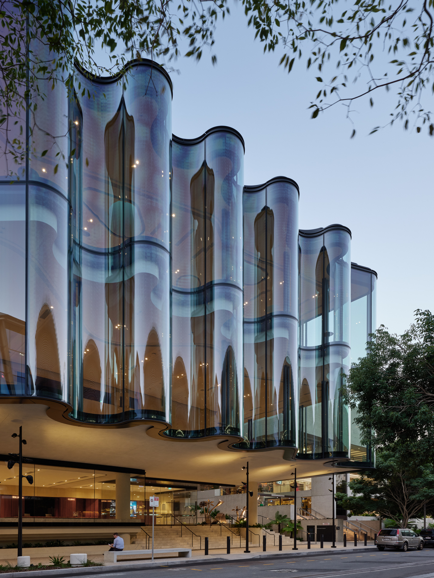 Side view of the cylindrical glass facade columns rising above the cantilevered podium at dusk