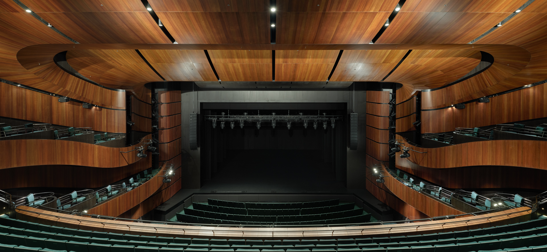 Symmetrical view of the theater auditorium showing timber balconies flanking the black proscenium stage
