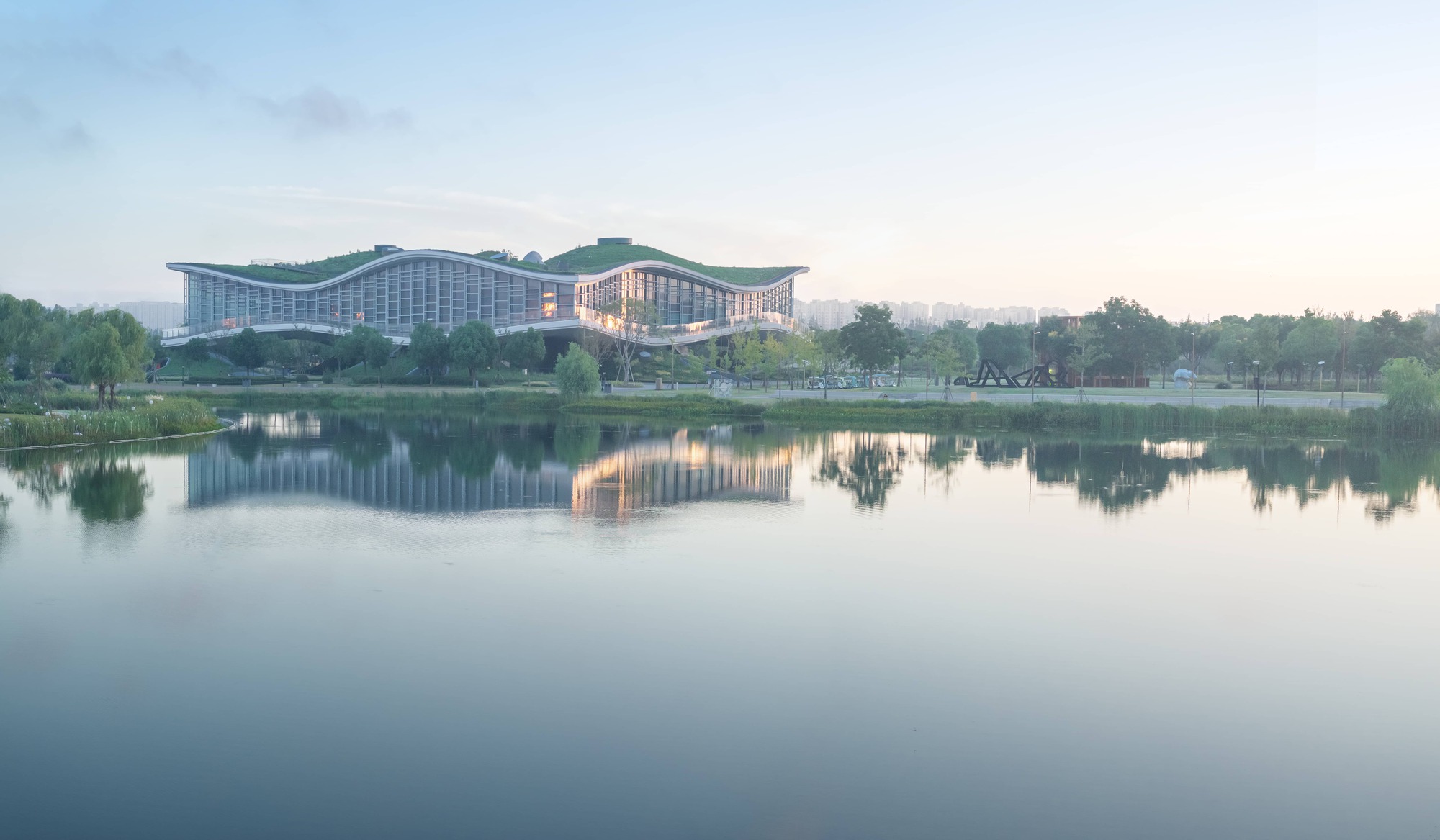 View across the lake showing the undulating green roof reflecting in still water at dawn