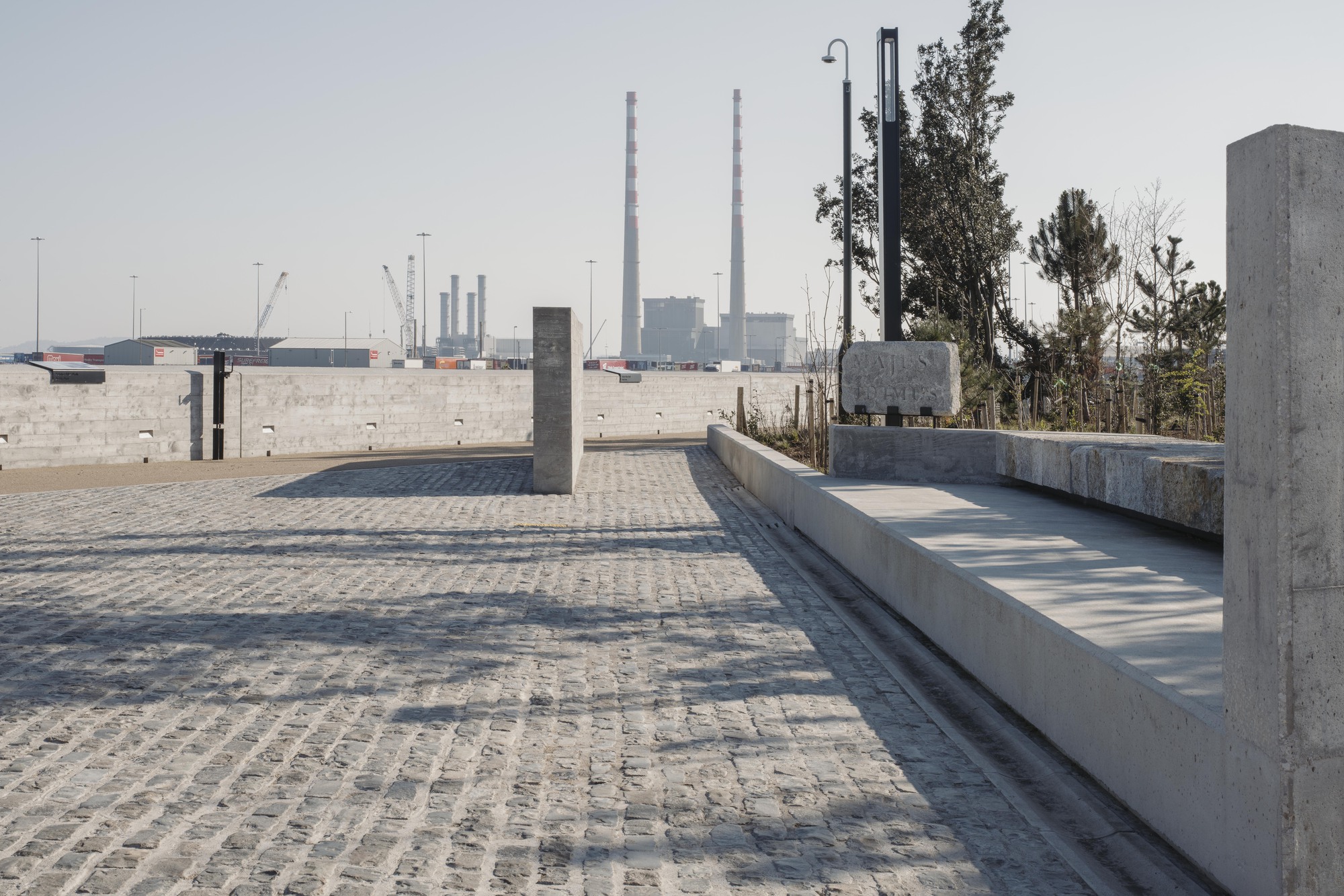 Granite block paving and concrete benches overlooking industrial harbor infrastructure in the distance