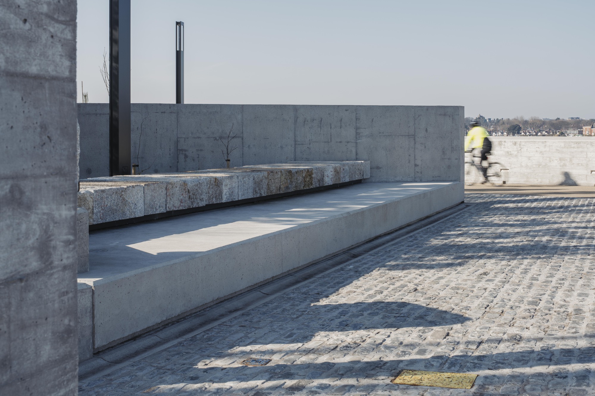 Cyclist in motion blur passing granite bench set into concrete terrace with metal posts