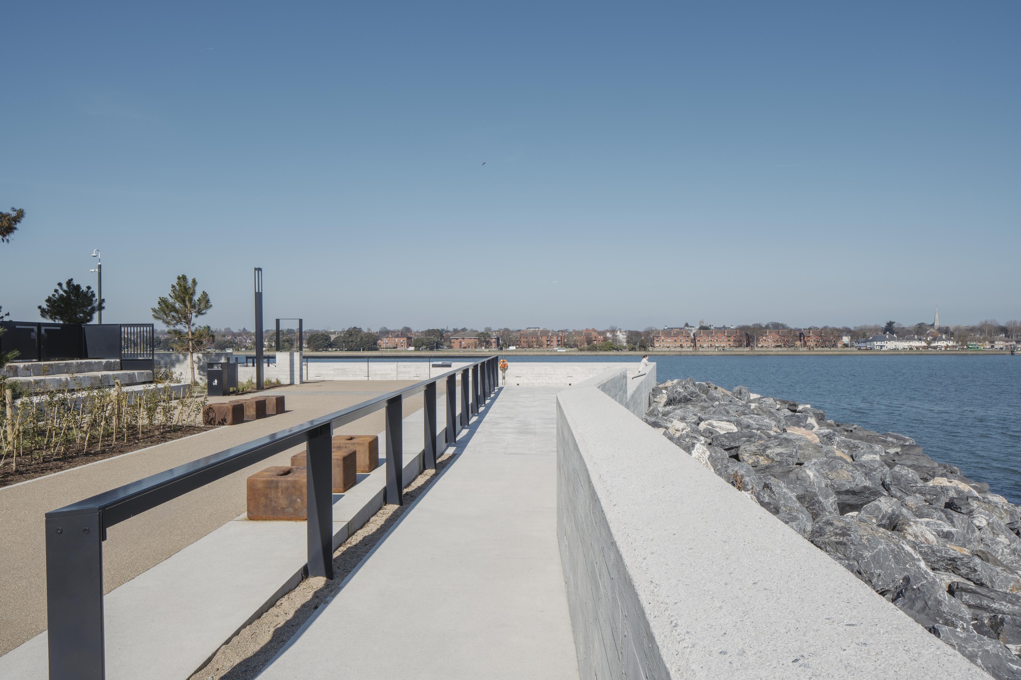 Waterfront promenade with timber benches between concrete walls and rocky shoreline