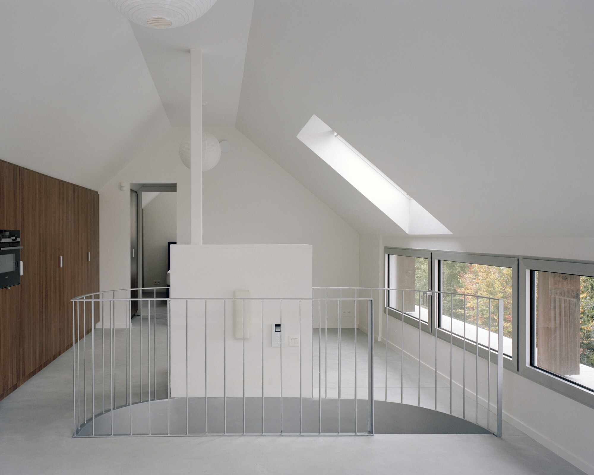 Top floor room with sloped ceiling, metal railing around stairwell opening, and skylight overhead