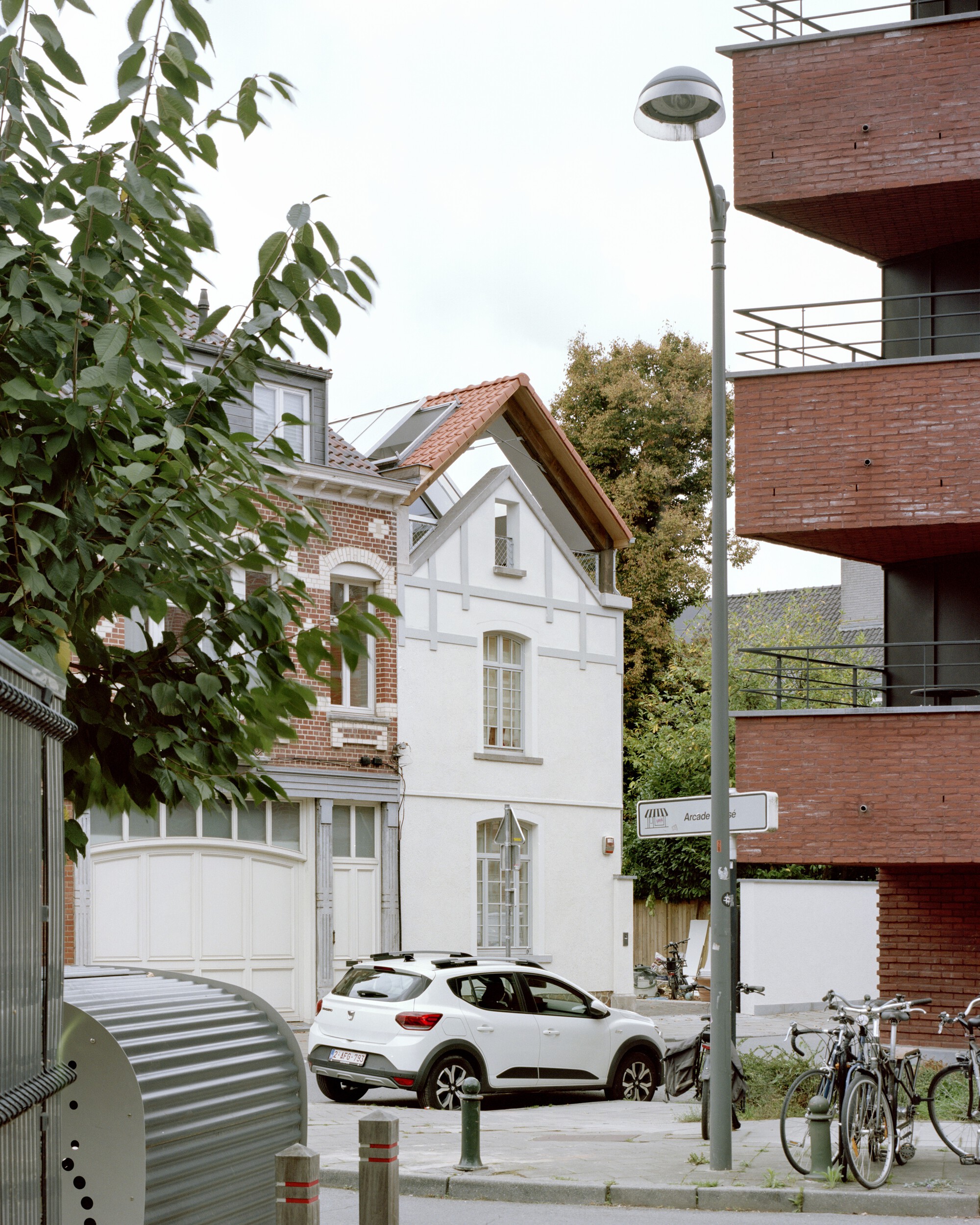 Street view of white rendered facade with gabled roof between brick neighbors and autumn trees