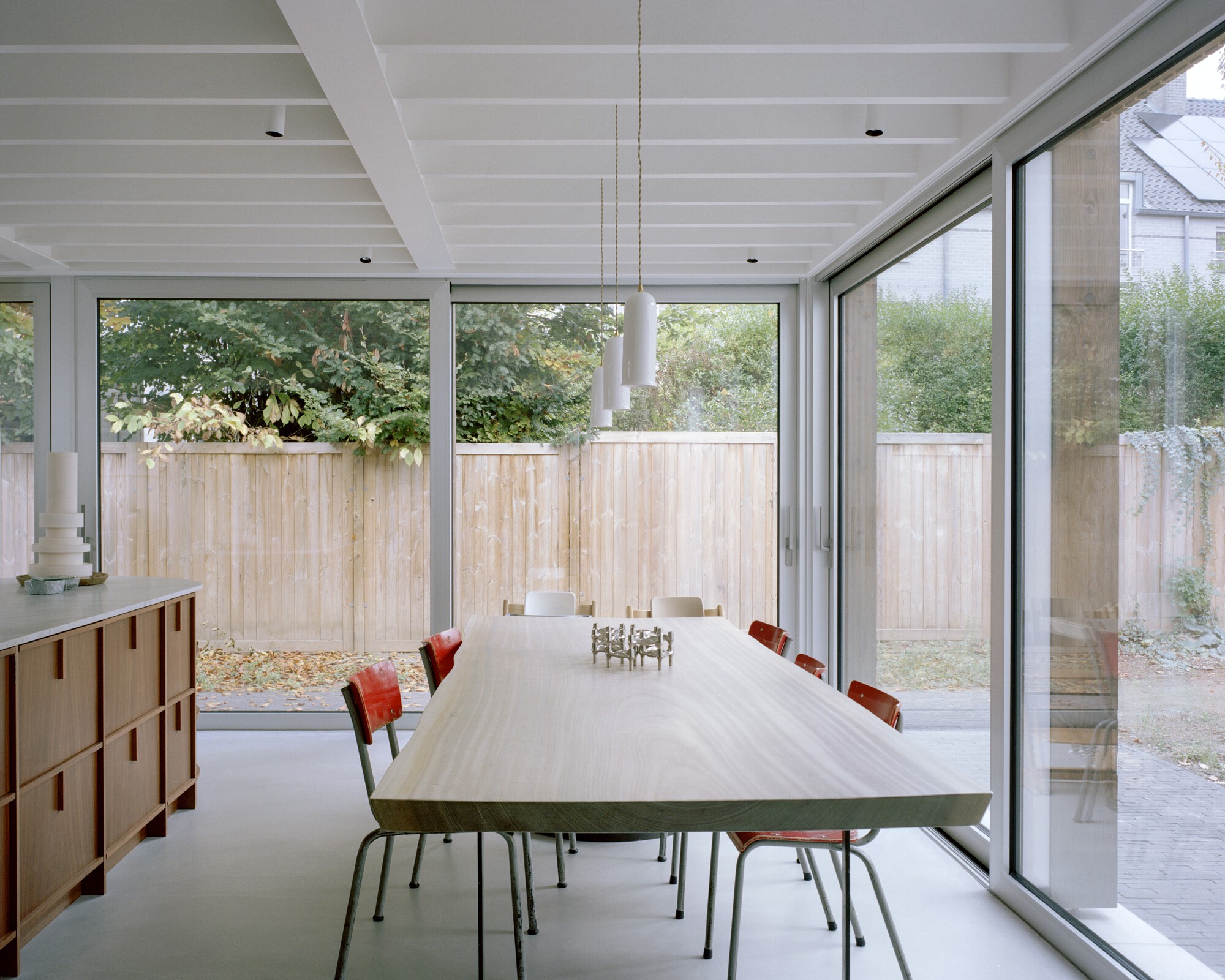 Dining area with white beamed ceiling and full-height glazing overlooking timber fence and garden