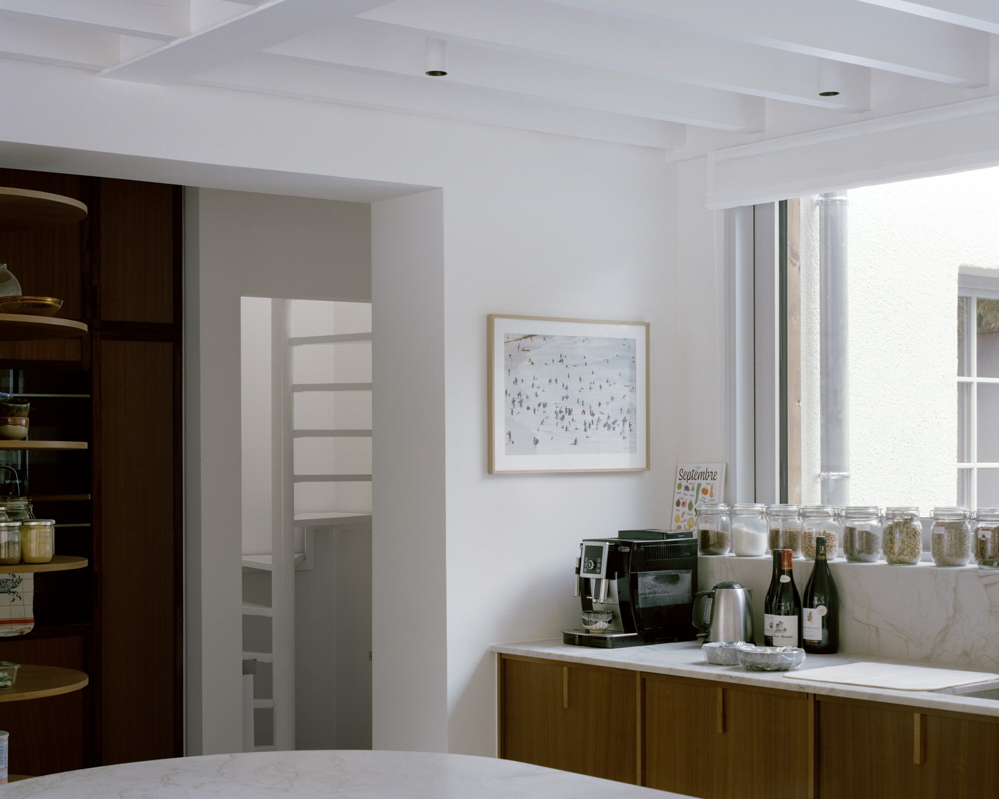 Kitchen with walnut cabinetry, white coffered ceiling and marble countertop under soft daylight