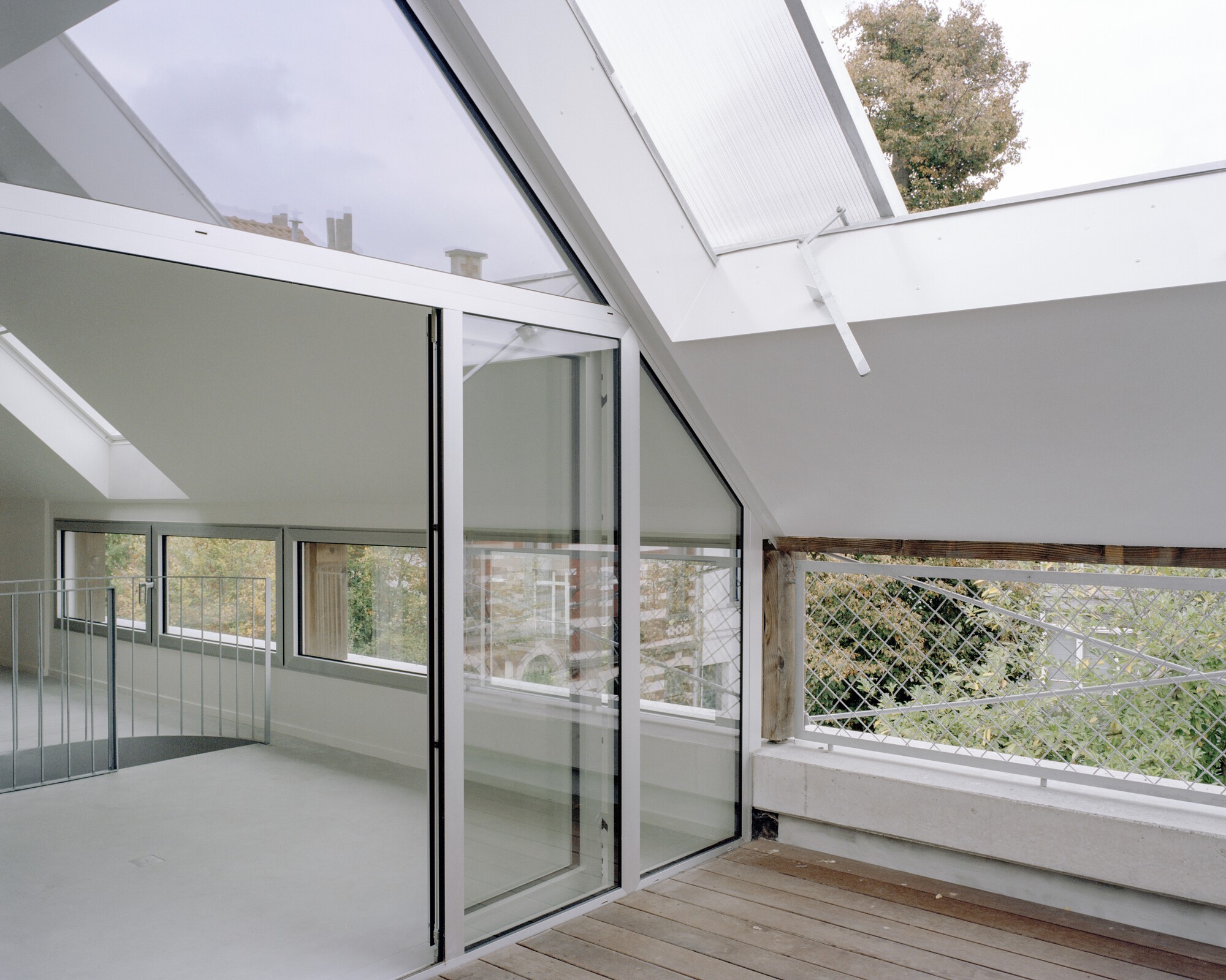 Roof terrace with timber decking, glazed sliding doors and wire mesh balustrade overlooking greenery