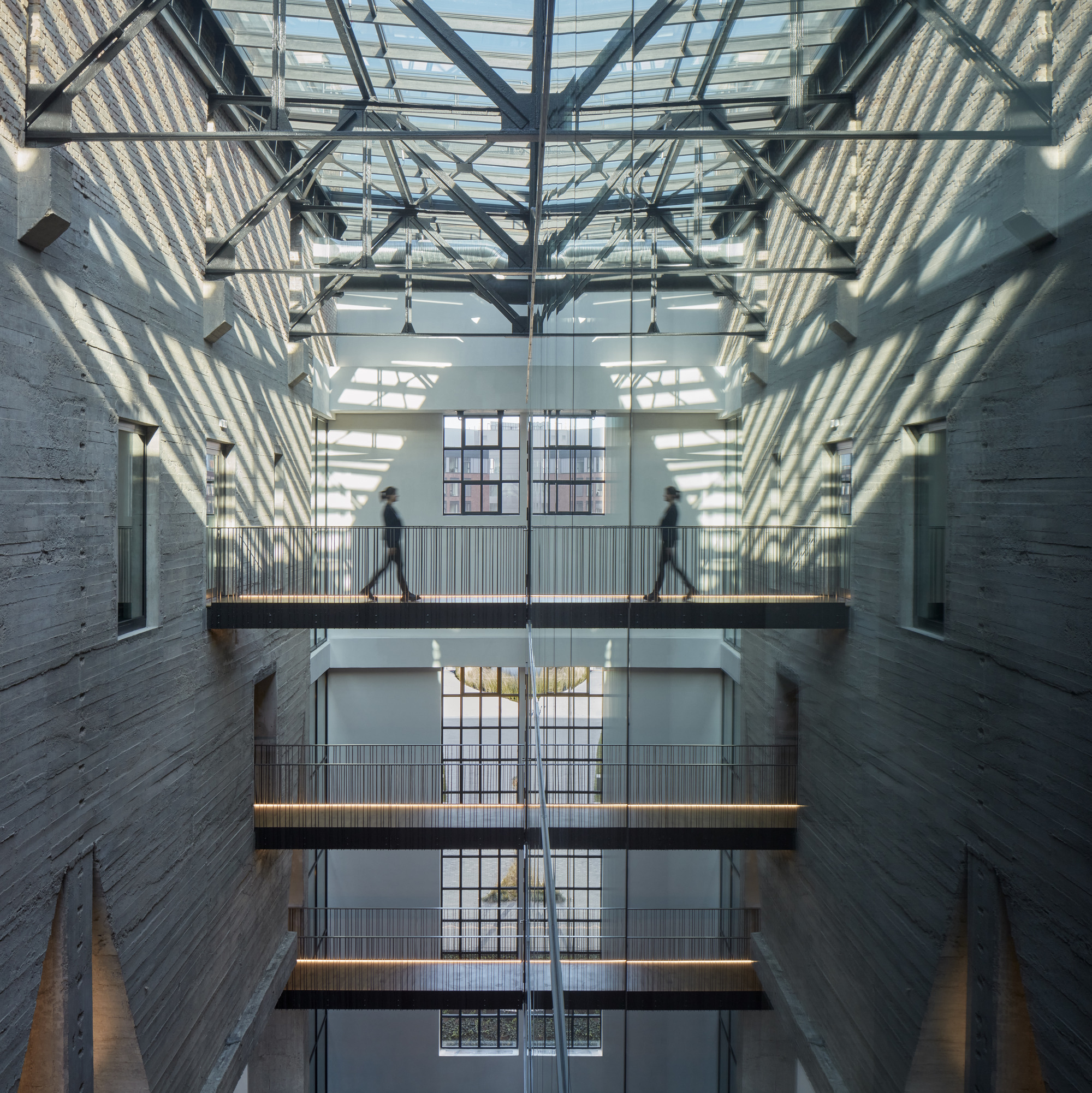 Upward view of stacked walkways with corrugated metal soffits casting geometric shadows through a skylight