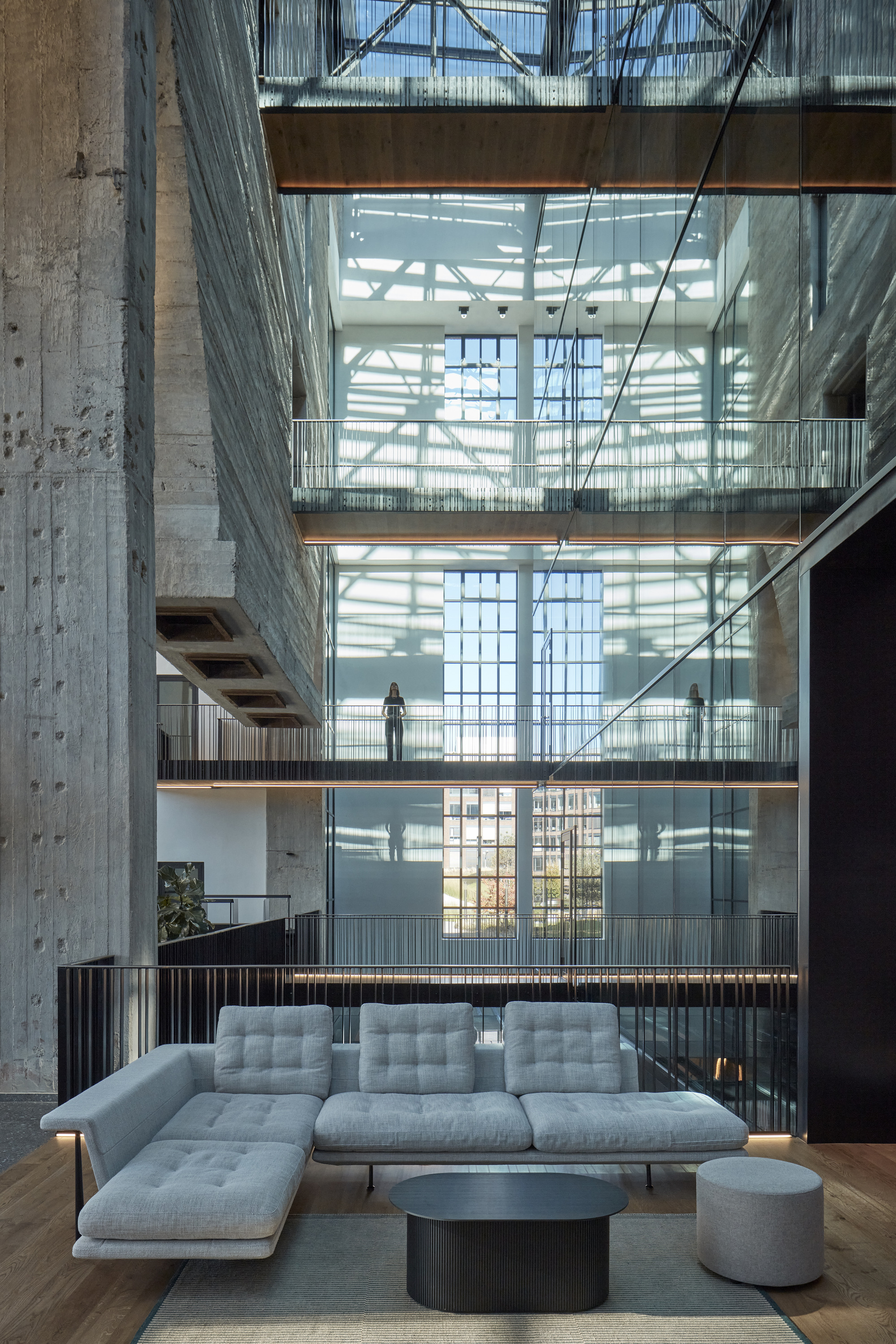 Lounge seating with sectional sofa facing a full-height atrium with walkways and a figure above
