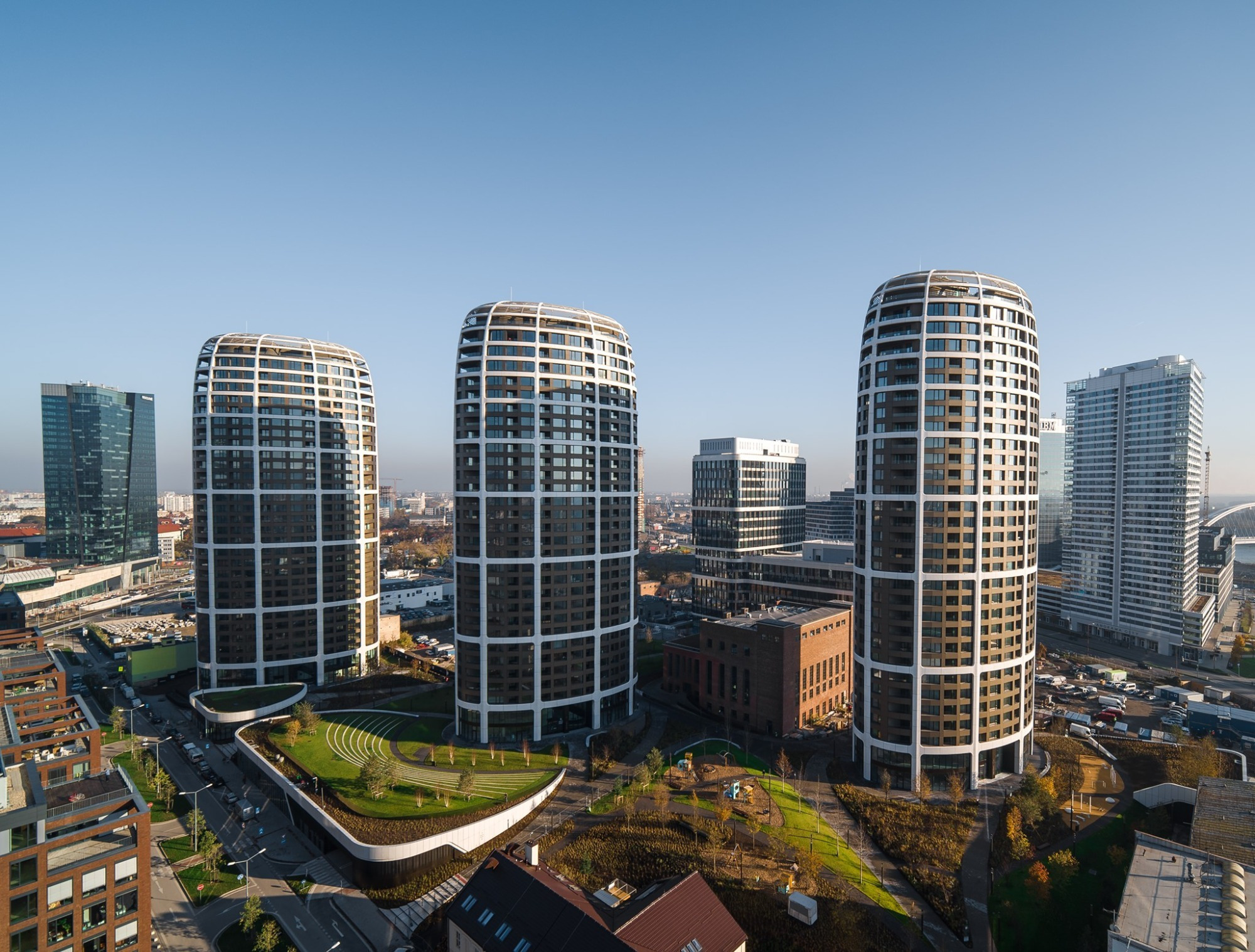Three cylindrical towers with horizontal banding overlooking a landscaped courtyard and neighboring buildings