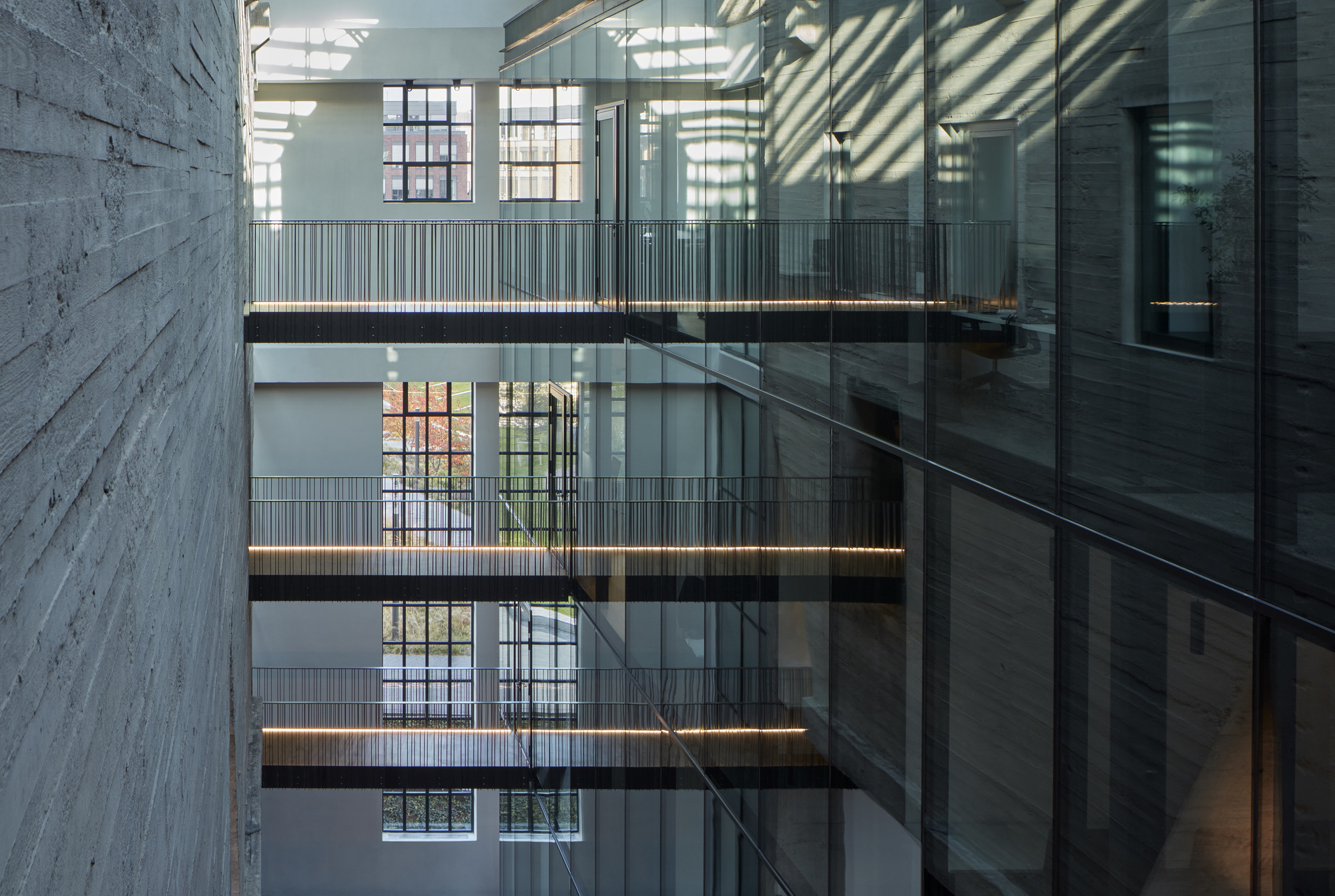 Interior atrium with stacked walkways and glass railings casting striped shadows across white walls